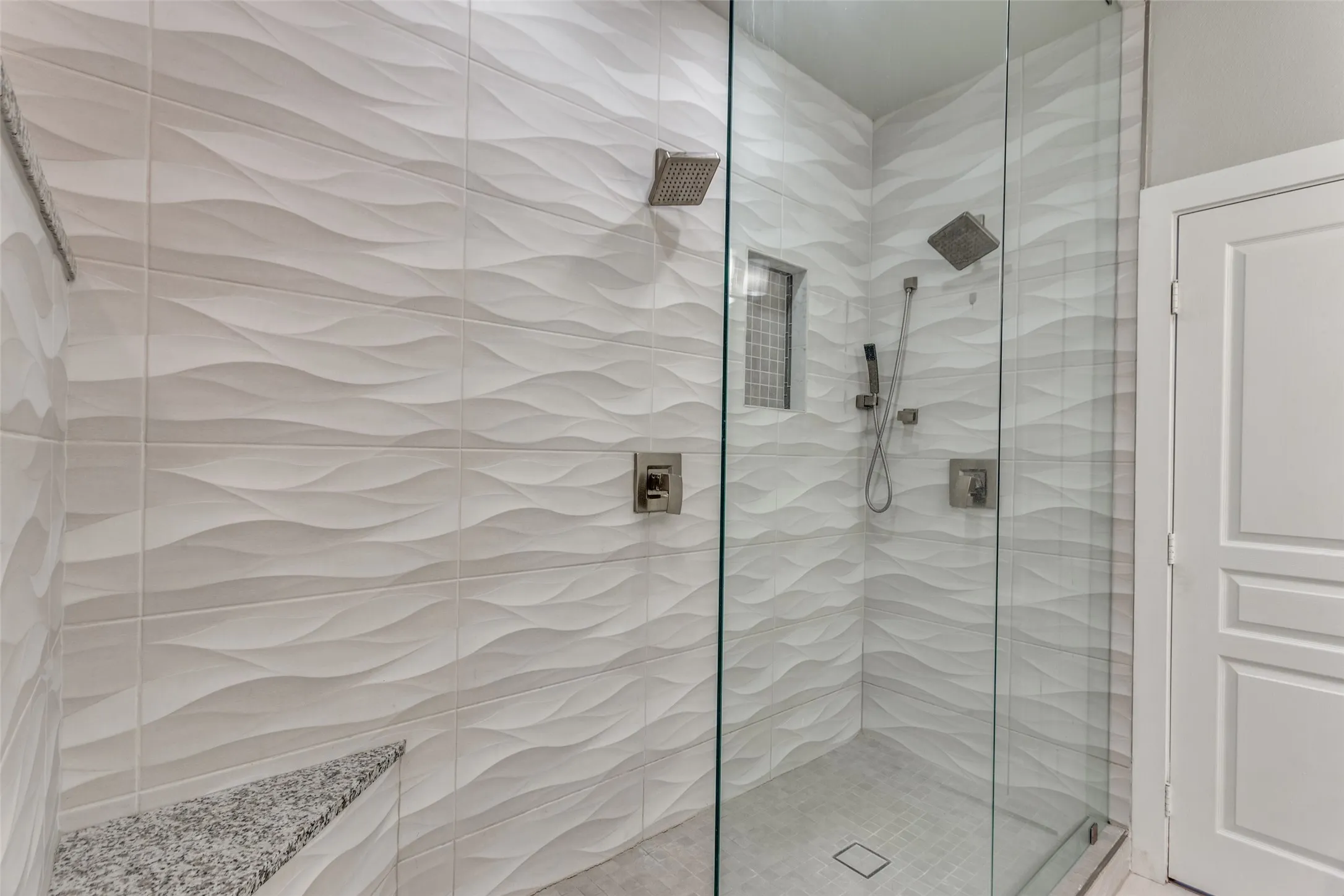 The extra large shower has a bench, a niche and 2 shower heads.