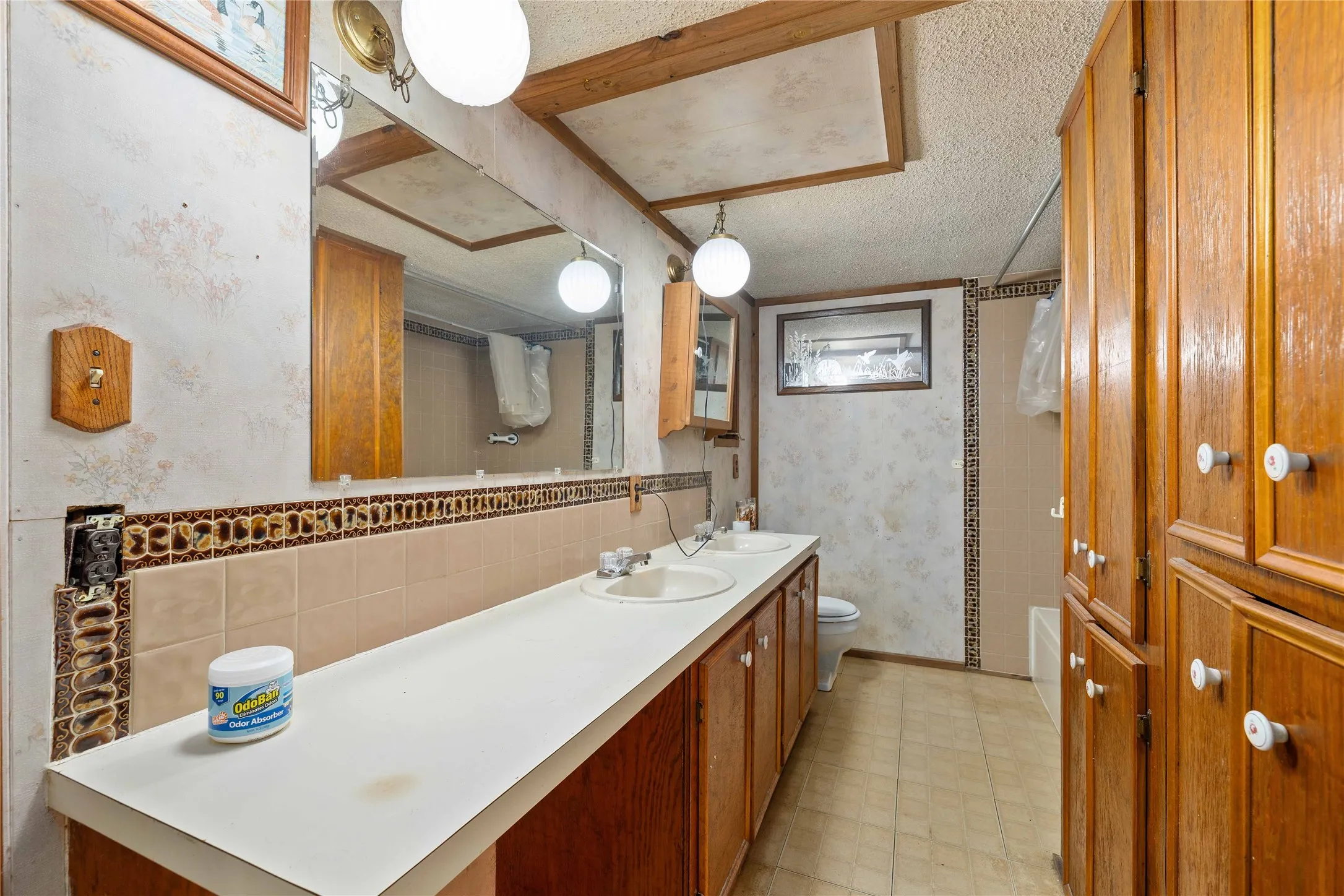 Full bathroom with wallpapered walls, double vanity, and a textured ceiling