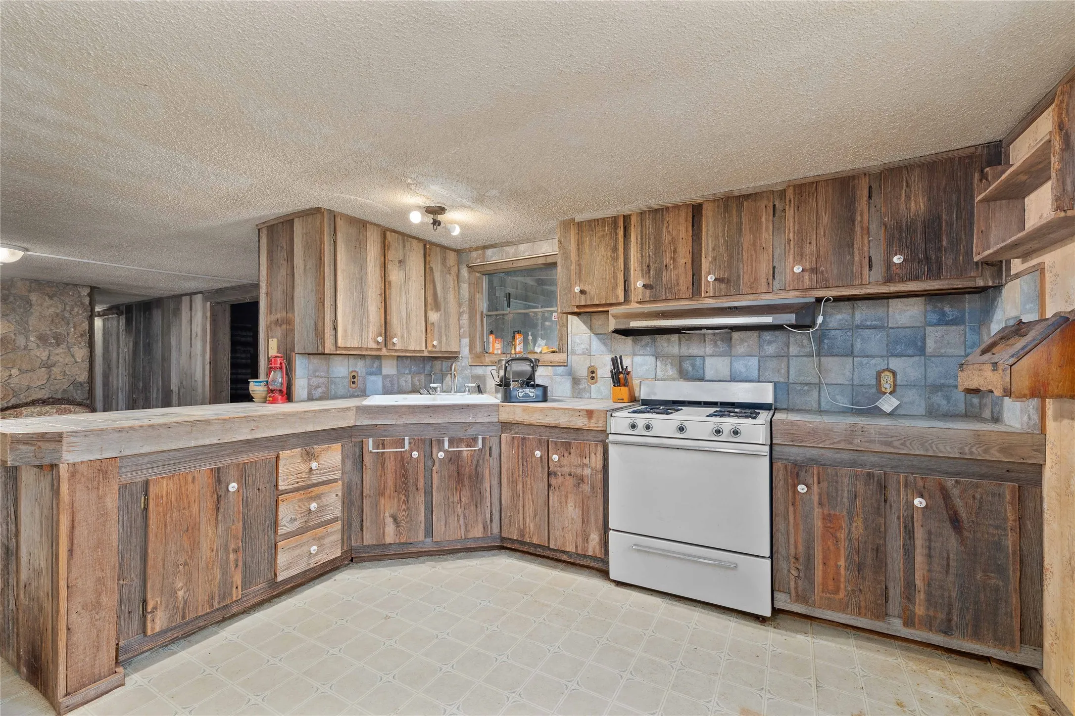 Kitchen featuring white range with gas stovetop, under cabinet range hood, light flooring, decorative backsplash, and a textured ceiling