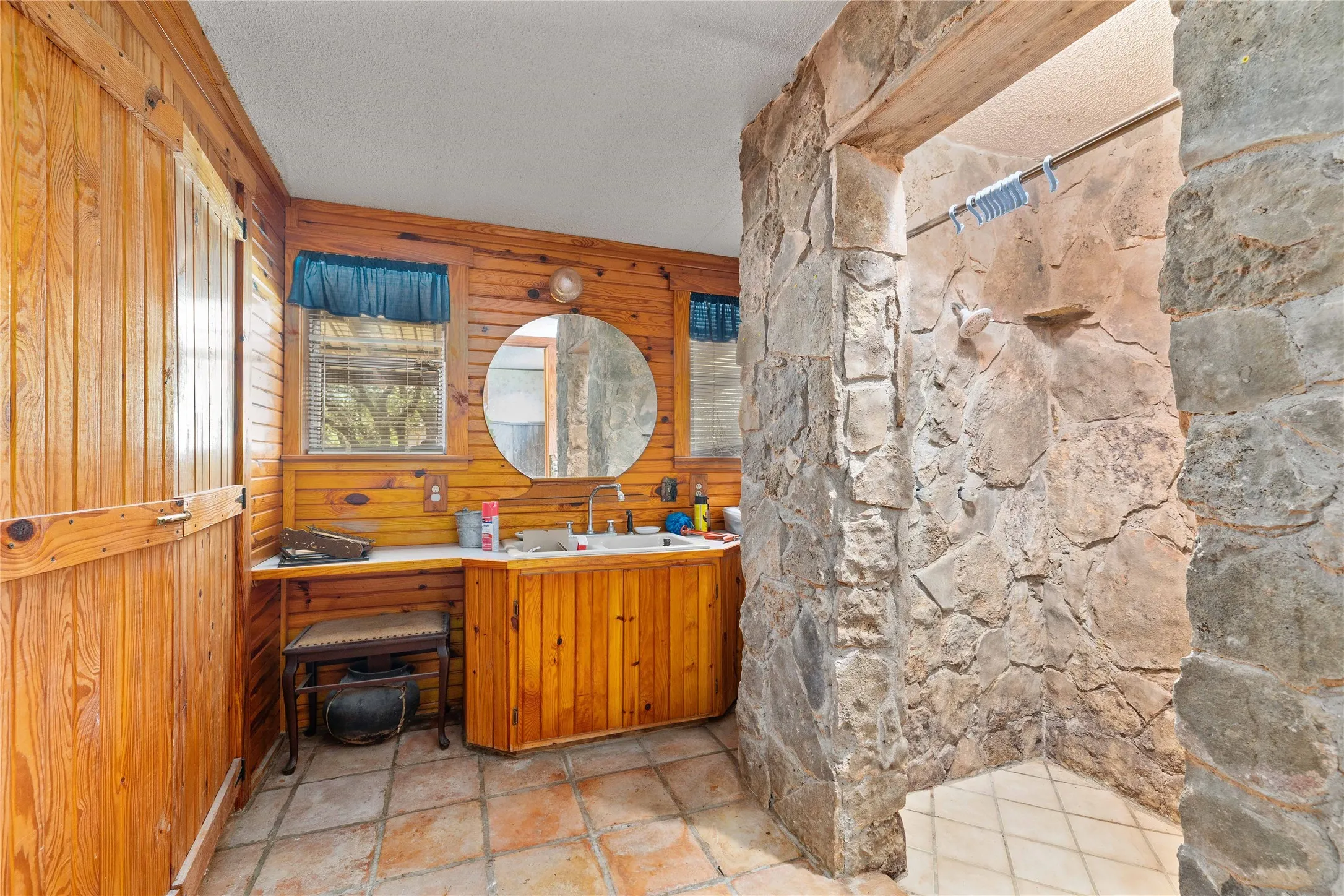 Full bath featuring wood walls, vanity, a shower, a textured ceiling, and stone finish floors