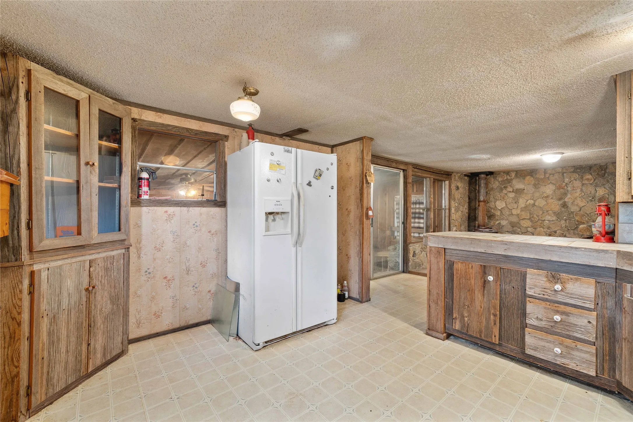 Kitchen featuring white fridge with ice dispenser, light floors, a textured ceiling, glass insert cabinets, and light countertops