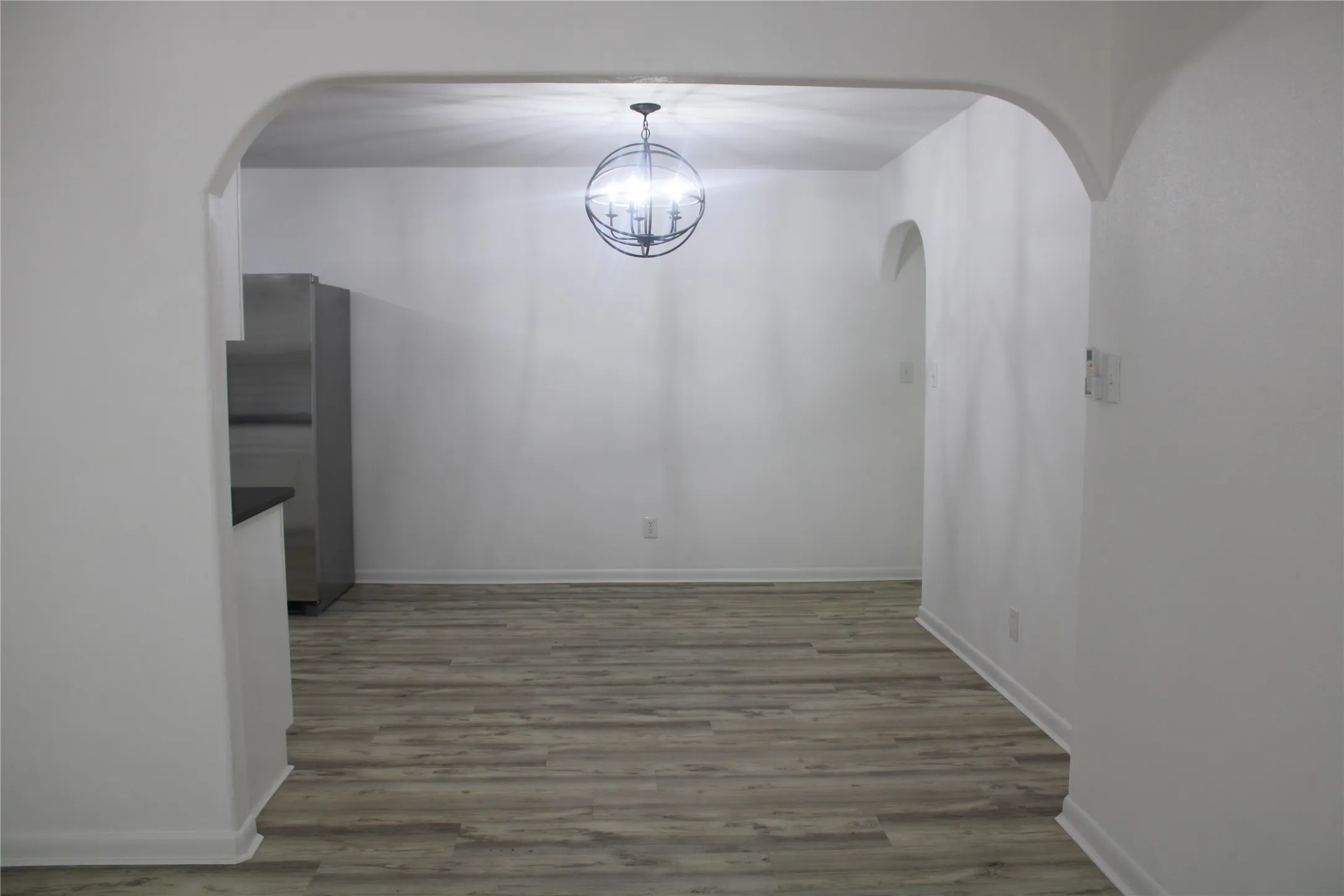 Unfurnished dining area with arched walkways, wood finished floors, and a chandelier