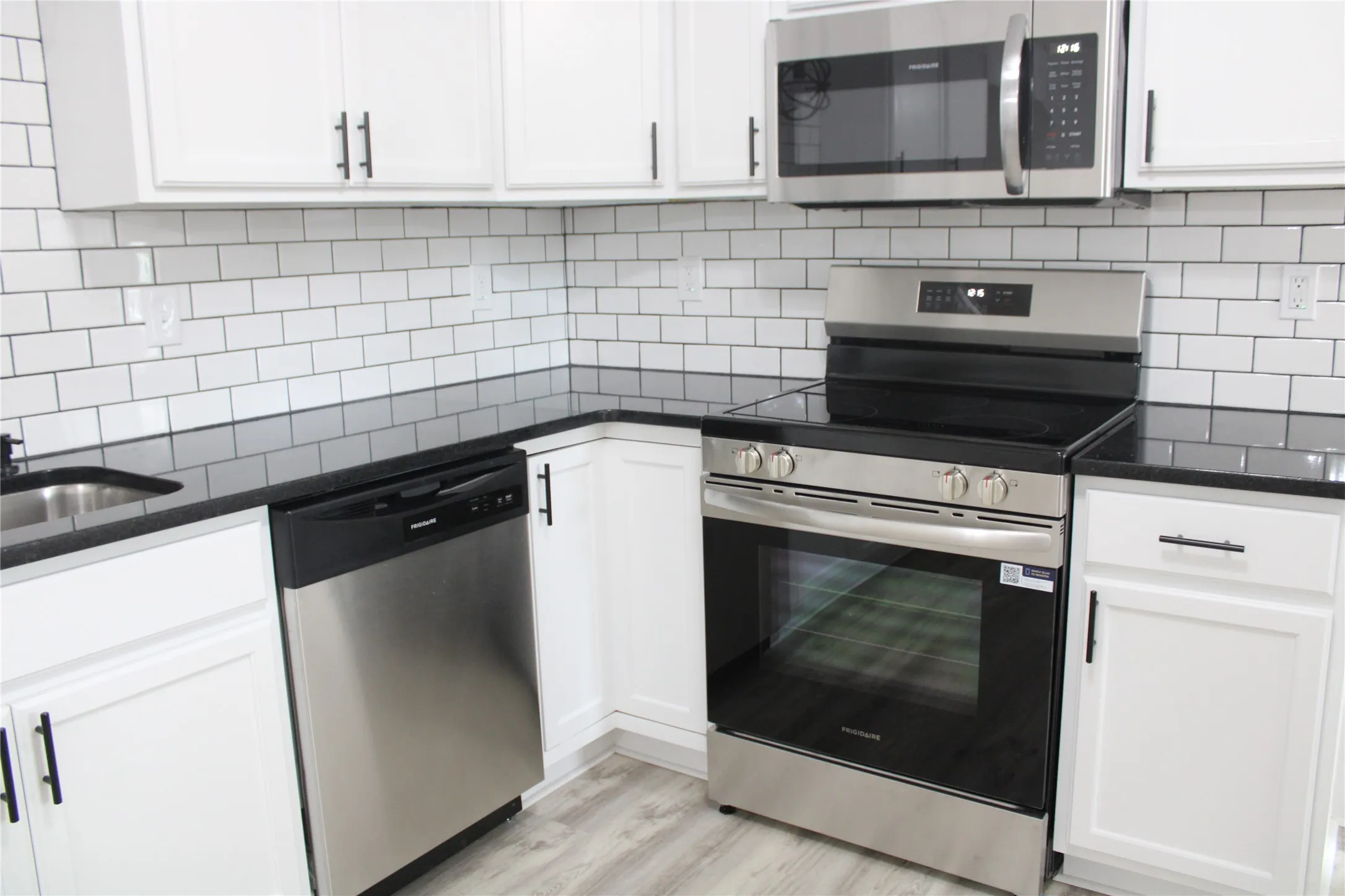 Kitchen with stainless steel appliances, white cabinetry, dark stone counters, and light wood-style flooring