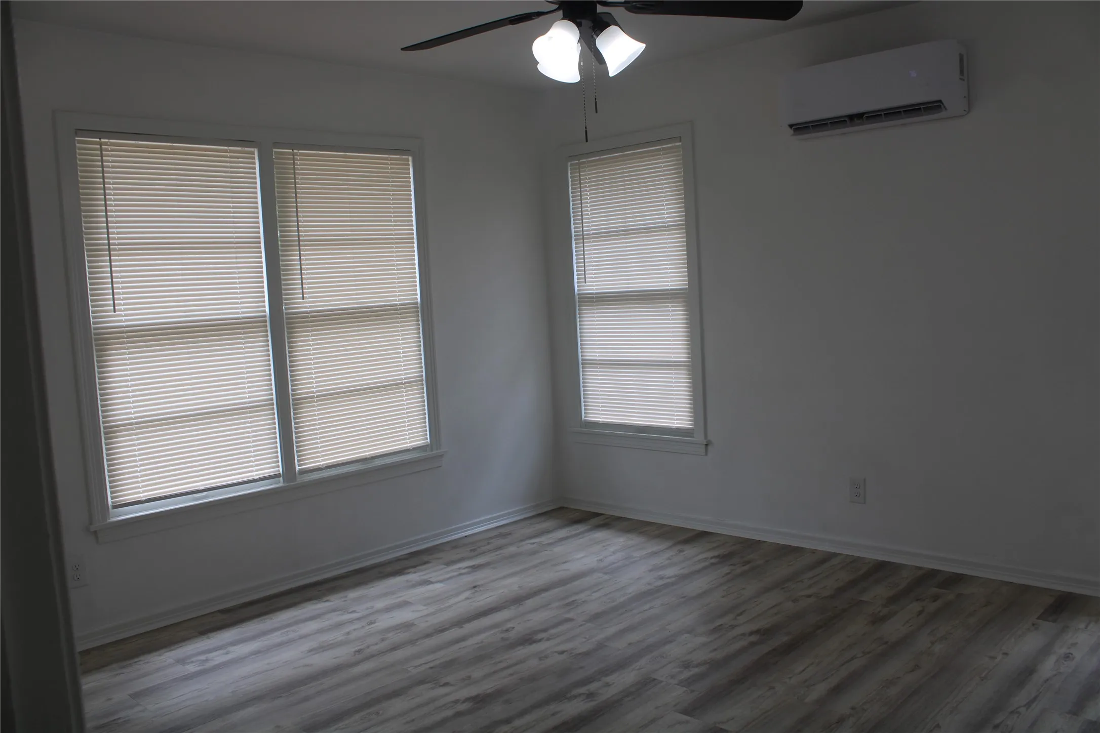 Unfurnished room with a wall unit AC, wood finished floors, and ceiling fan