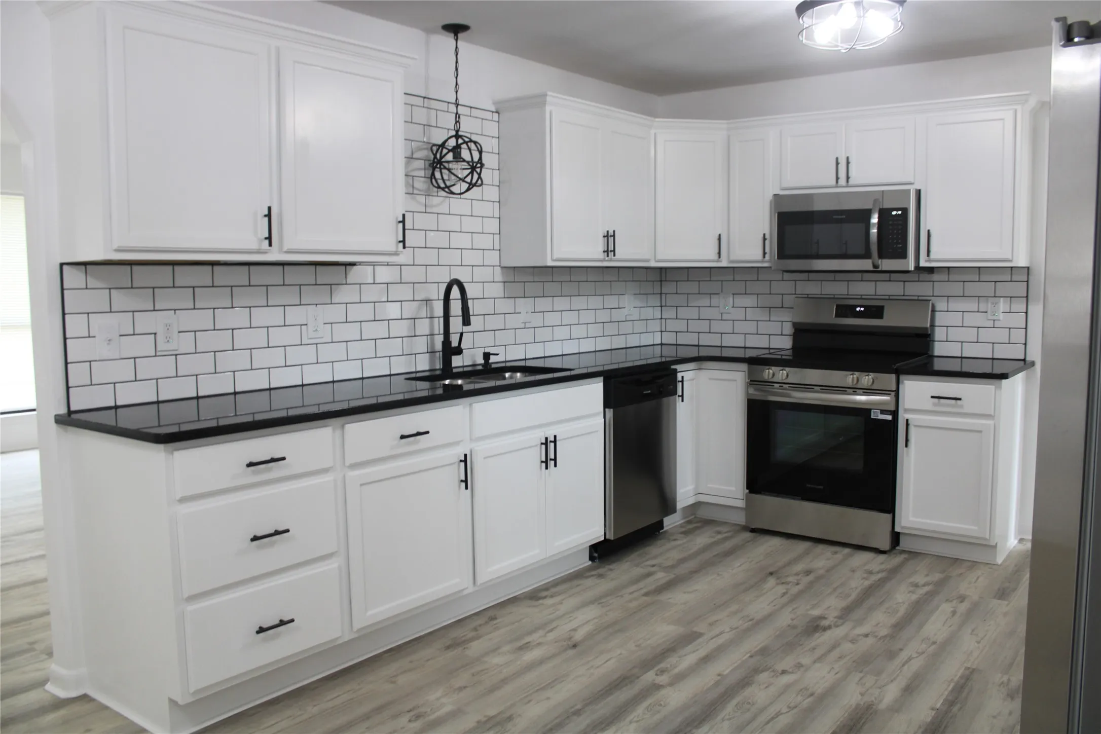 Kitchen featuring appliances with stainless steel finishes, light wood-style floors, white cabinets, dark countertops, and backsplash