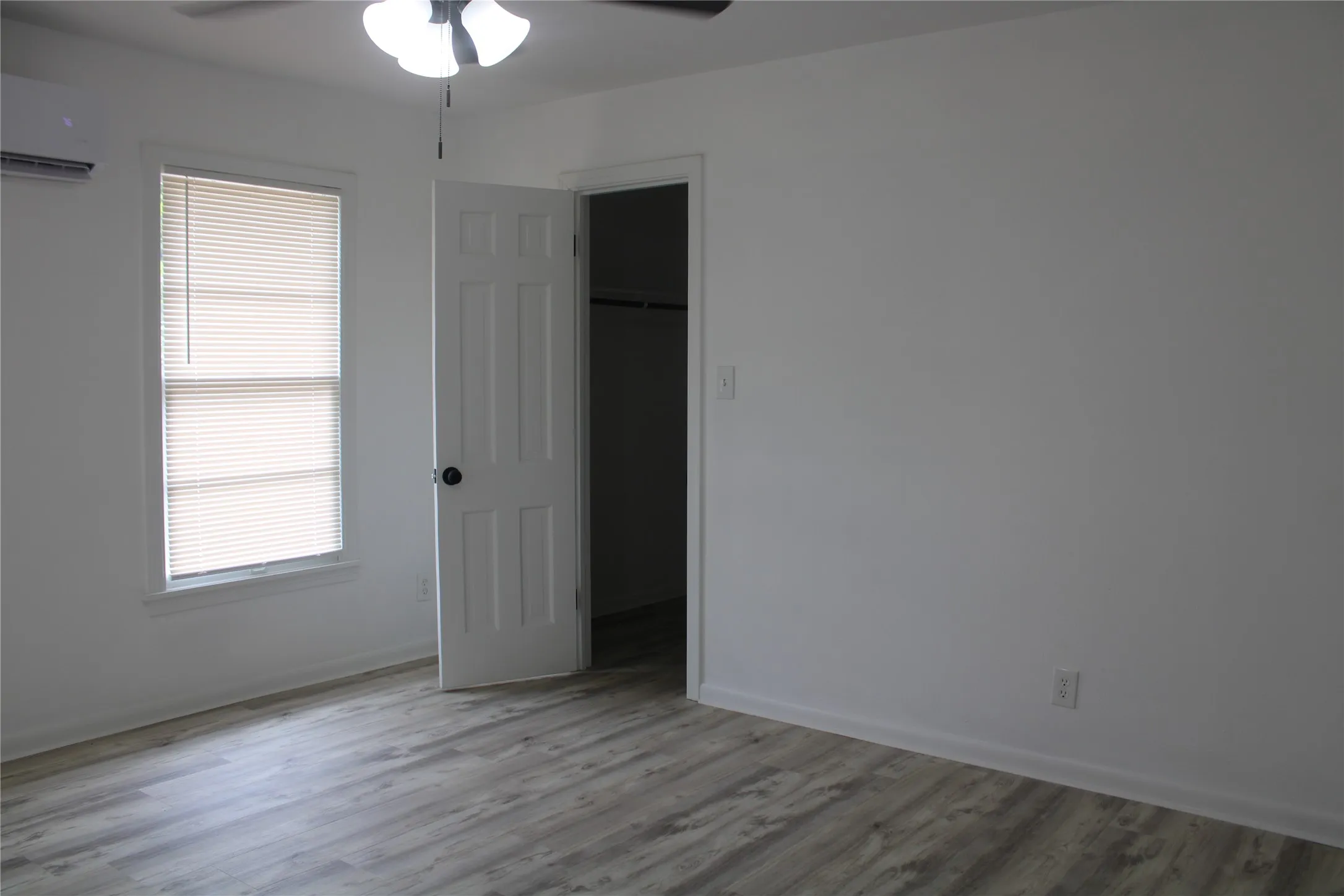 Unfurnished bedroom featuring an AC wall unit, wood finished floors, a walk in closet, and ceiling fan