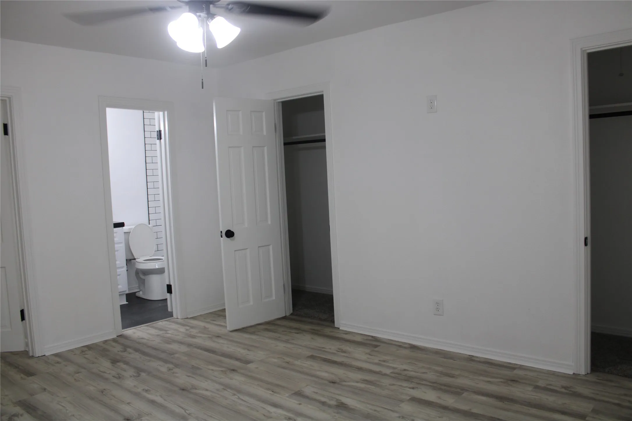 Unfurnished bedroom with a spacious closet, wood finished floors, ensuite bath, and ceiling fan