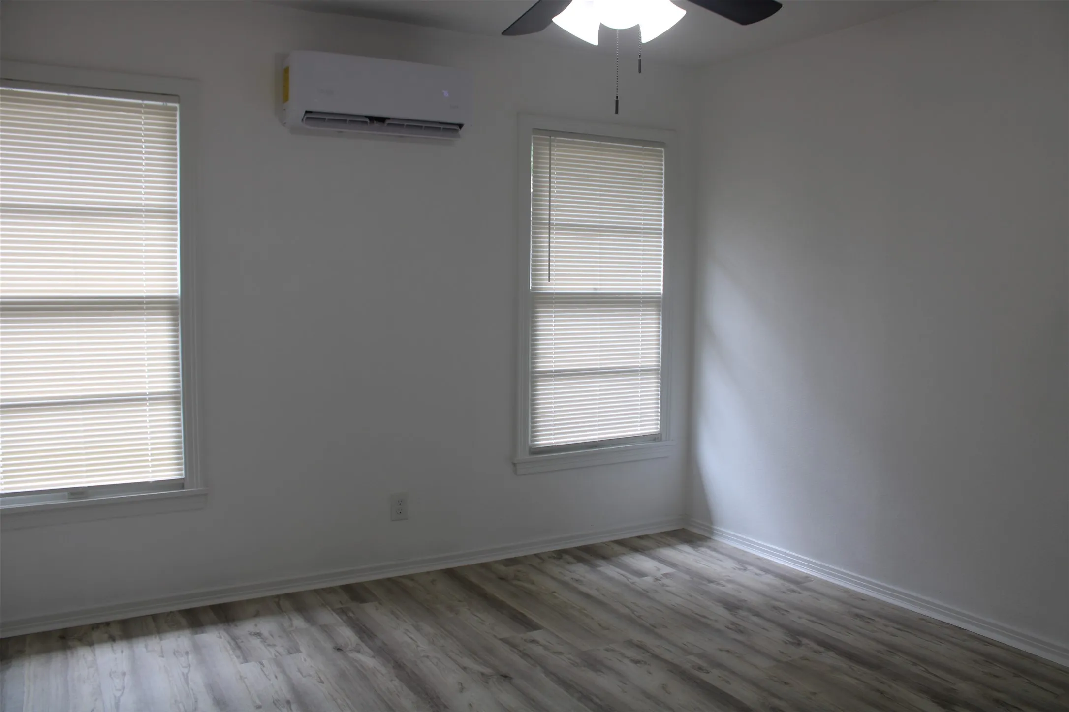 Spare room with a wall unit AC, wood finished floors, ceiling fan, and plenty of natural light