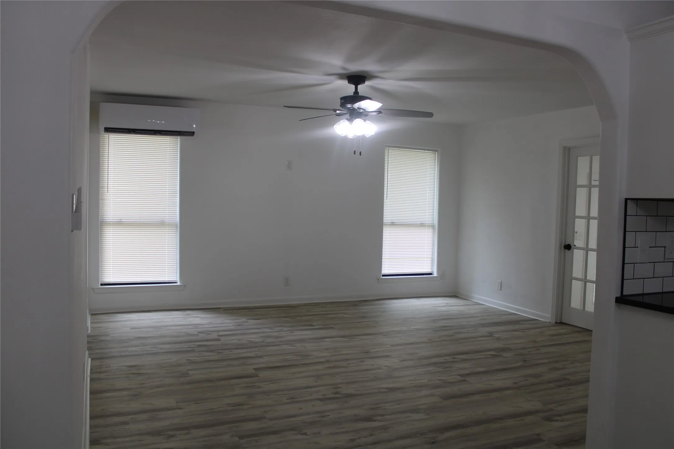 Empty room featuring arched walkways, ceiling fan, wood finished floors, and an AC wall unit