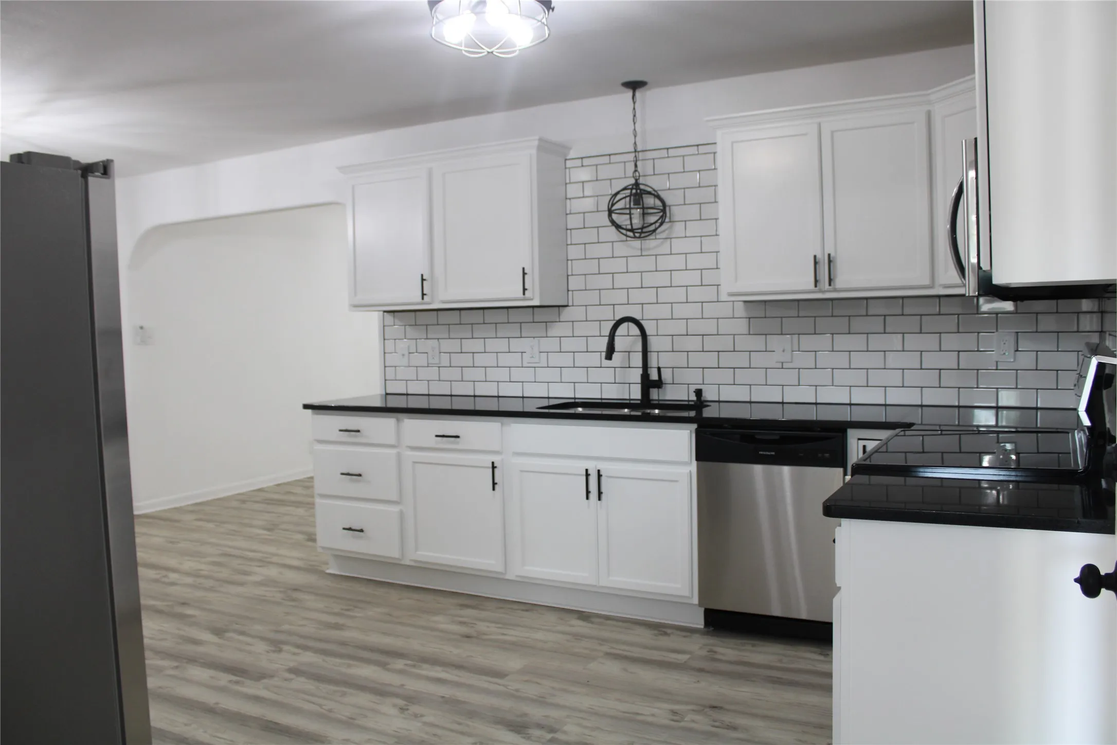 Kitchen featuring stainless steel appliances, dark countertops, decorative backsplash, and white cabinetry