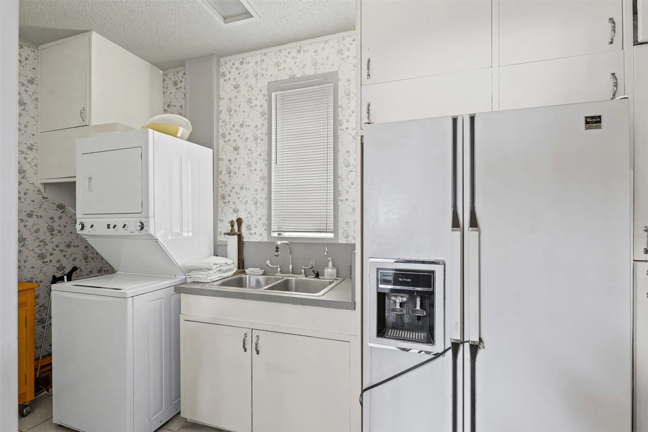 Laundry area featuring estacked washer and dryer, wallpapered walls, and a textured ceiling