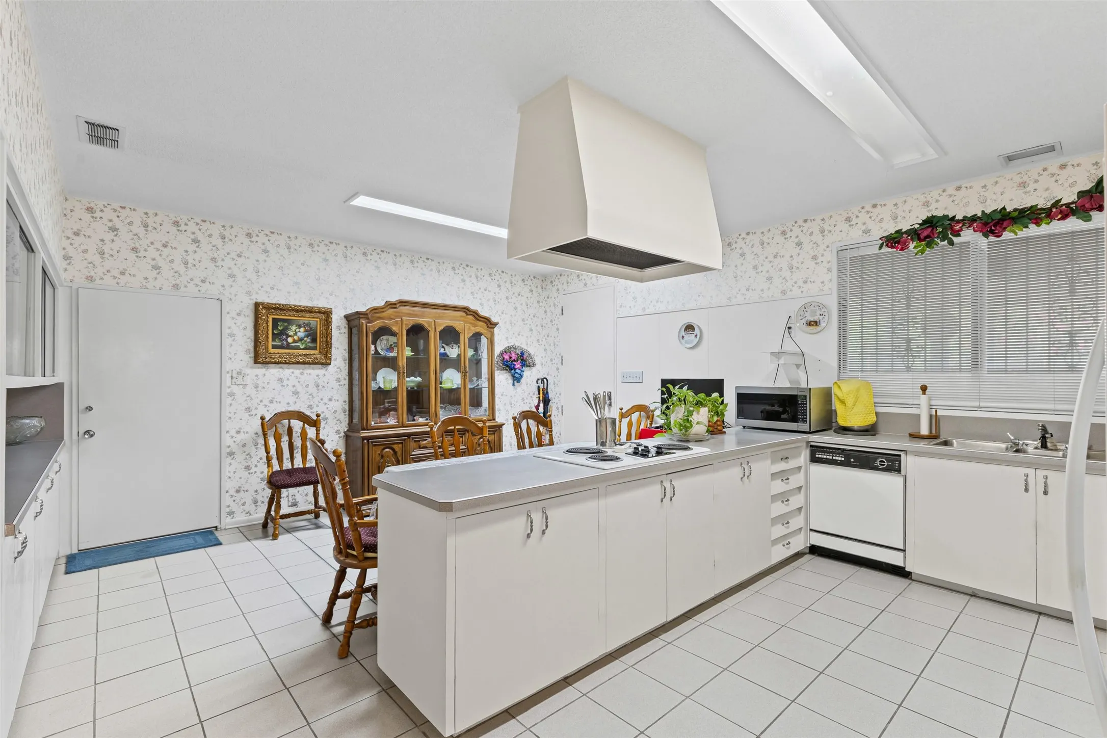 Kitchen with wallpapered walls, a peninsula, light tile patterned flooring, white cabinetry, and white appliances