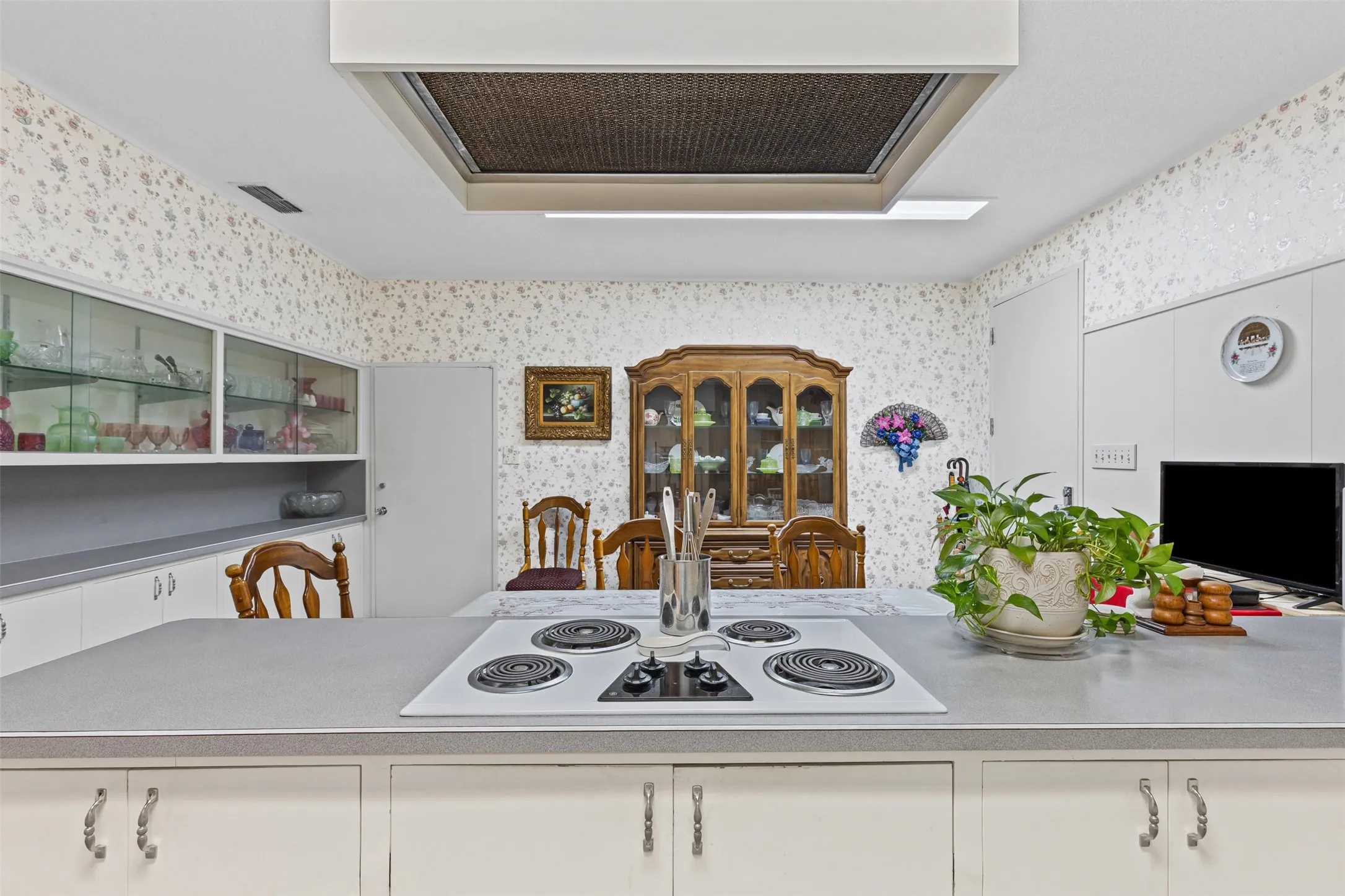 Kitchen featuring wallpapered walls, ventilation hood, white electric cooktop, and white cabinetry