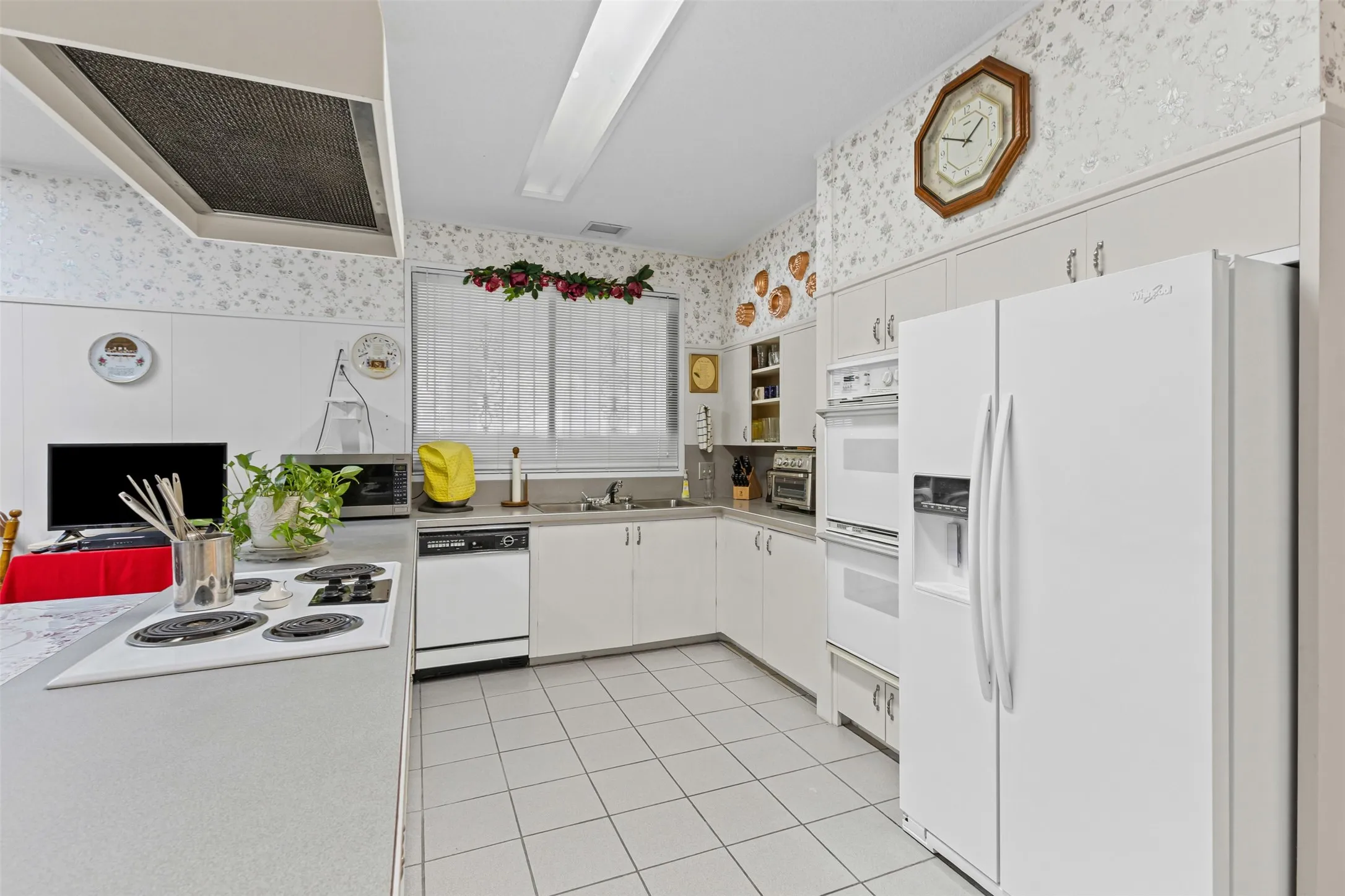 Kitchen featuring wallpapered walls, white appliances, exhaust hood, light tile patterned floors, and white cabinetry