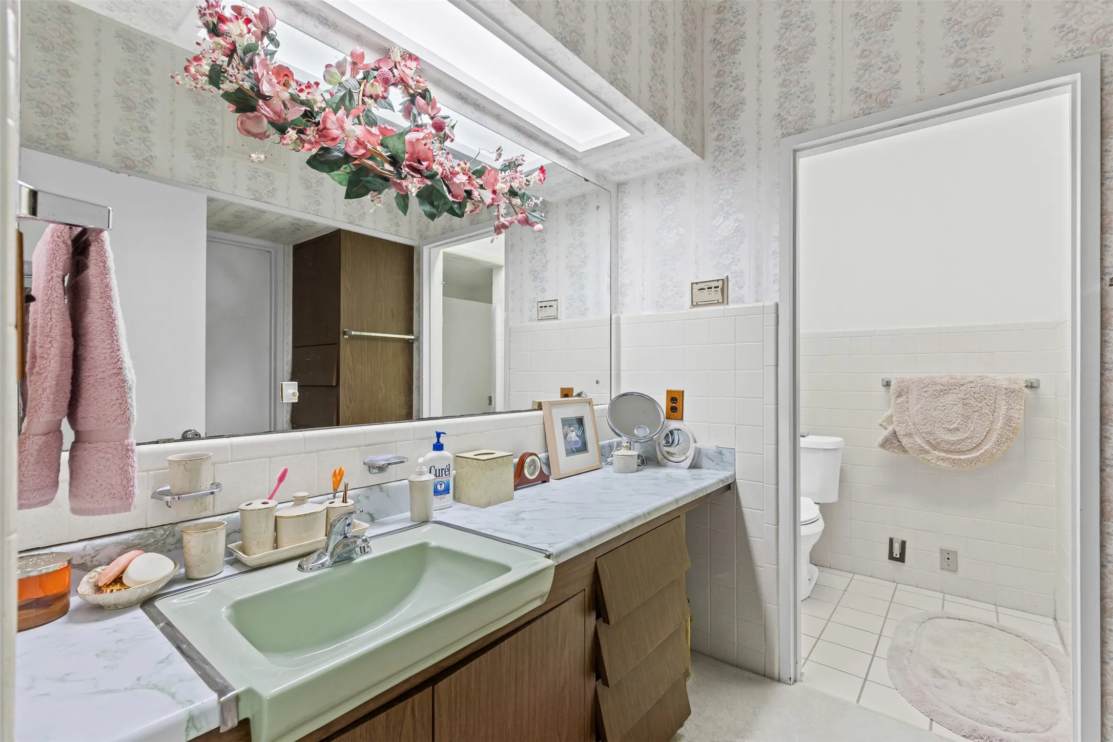 Bathroom with wallpapered walls, vanity, wainscoting, tile patterned floors, and tile walls