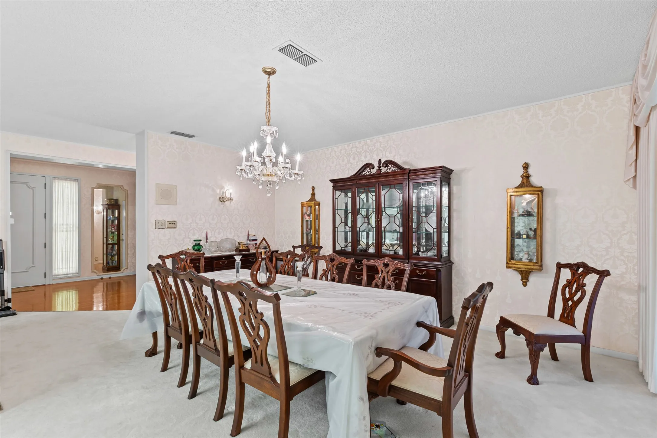 Dining room featuring light colored carpet, a chandelier, and wallpapered walls