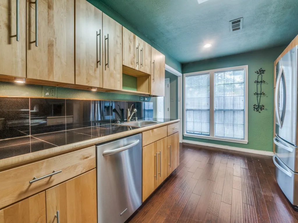 Kitchen with stainless steel appliances , light brown cabinets, dark wood-style flooring, and a textured ceiling