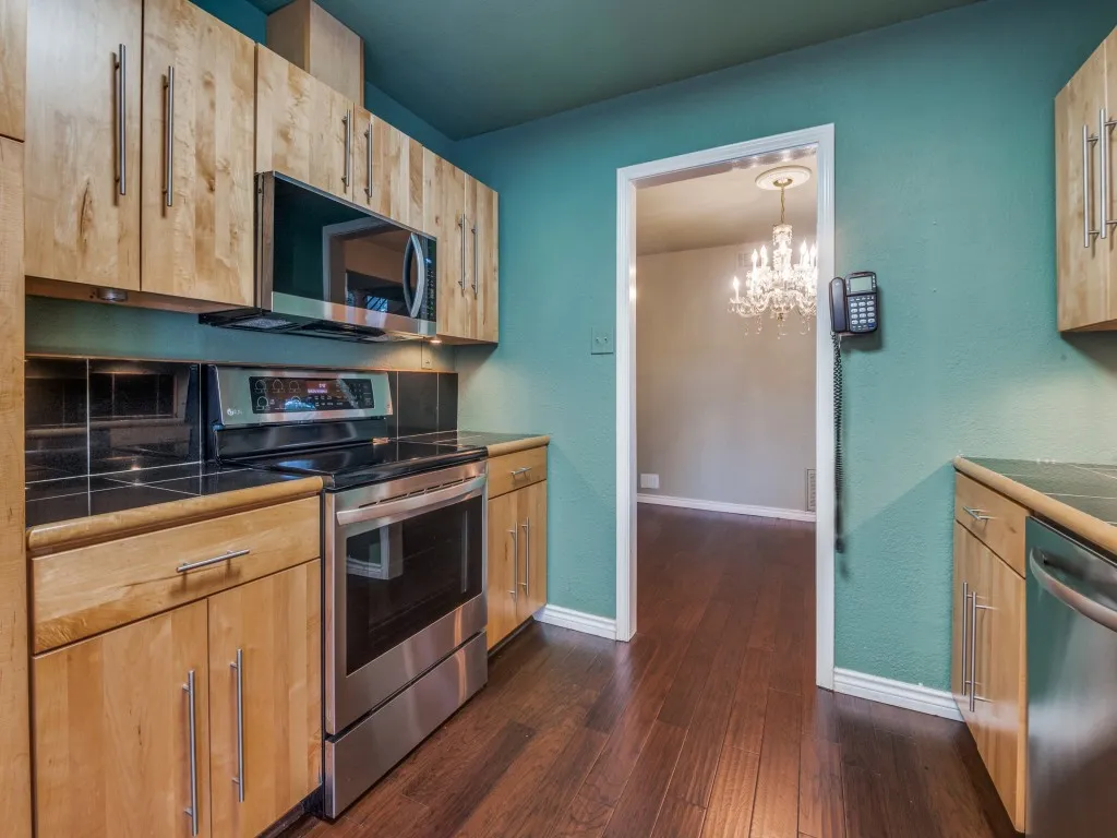 Kitchen with stainless steel appliances, dark wood-type flooring, light brown cabinetry, a chandelier, and dark countertops