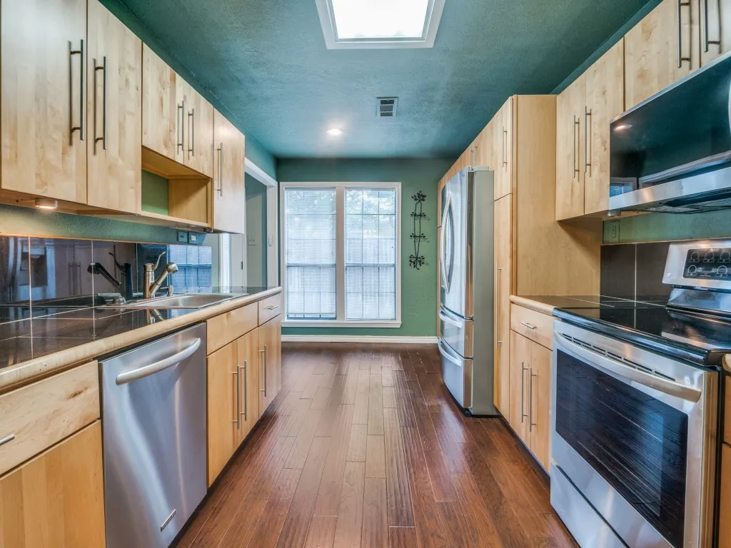 Kitchen stainless steel appliances, modern, custom light brown cabinets, dark wood-type flooring, and a textured ceiling