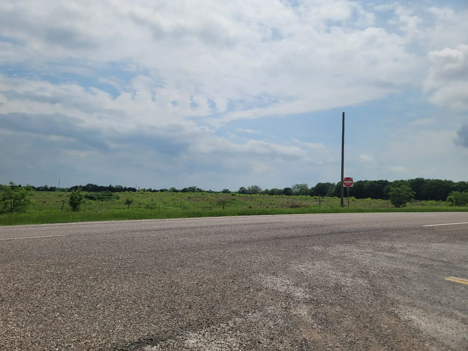 View of asphalt street with a view of rural / pastoral area and traffic signs