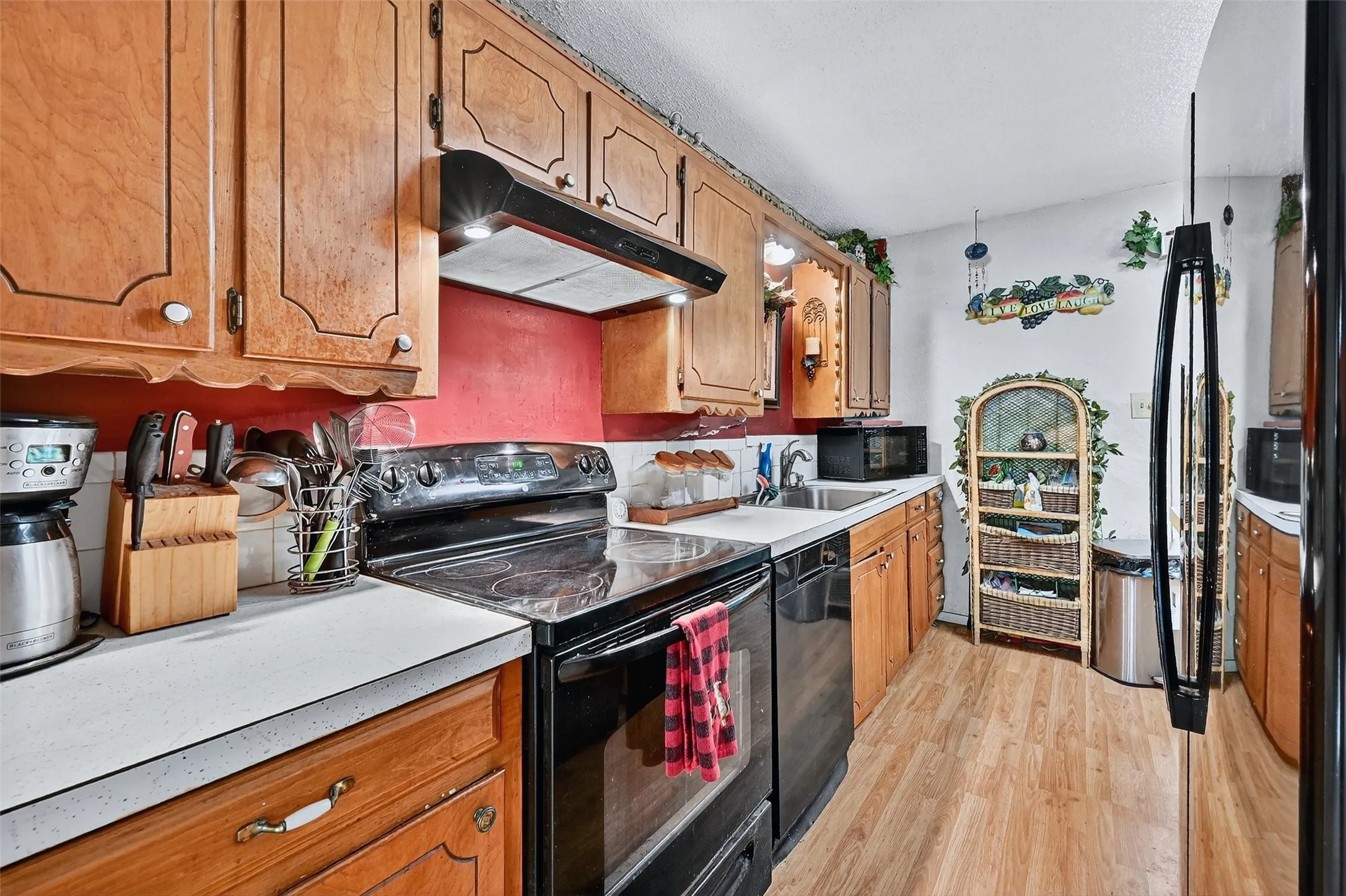 Kitchen with under cabinet range hood, black appliances, light wood-type flooring, and light countertops