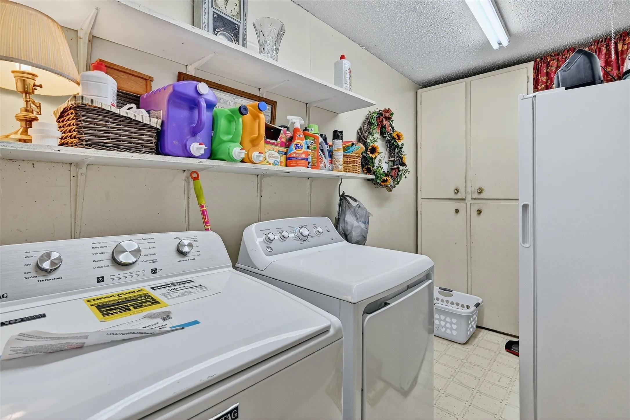 Laundry area with cabinet space, independent washer and dryer, light flooring, and a textured ceiling
