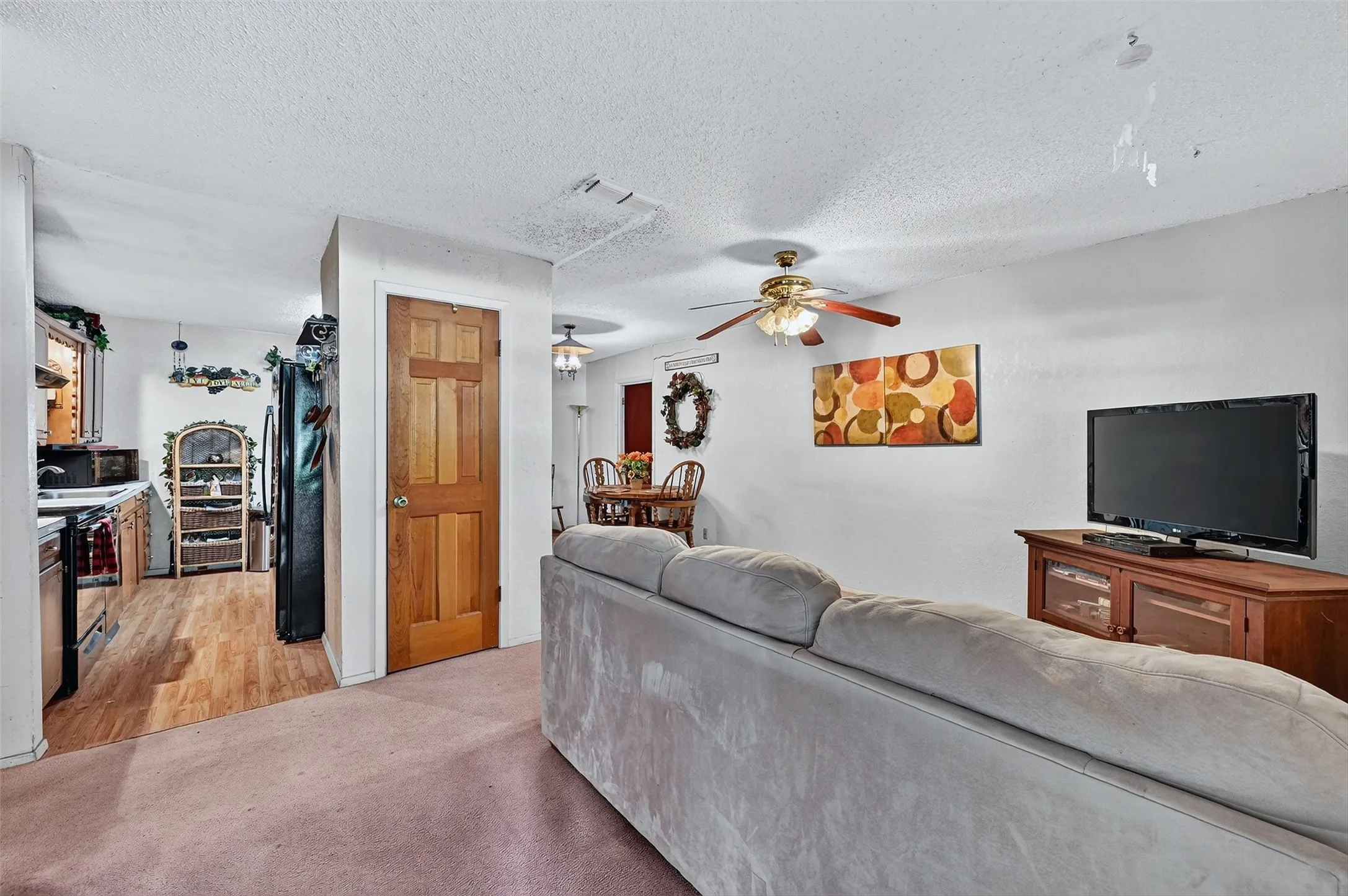 Living area featuring a ceiling fan, light carpet, and a textured ceiling