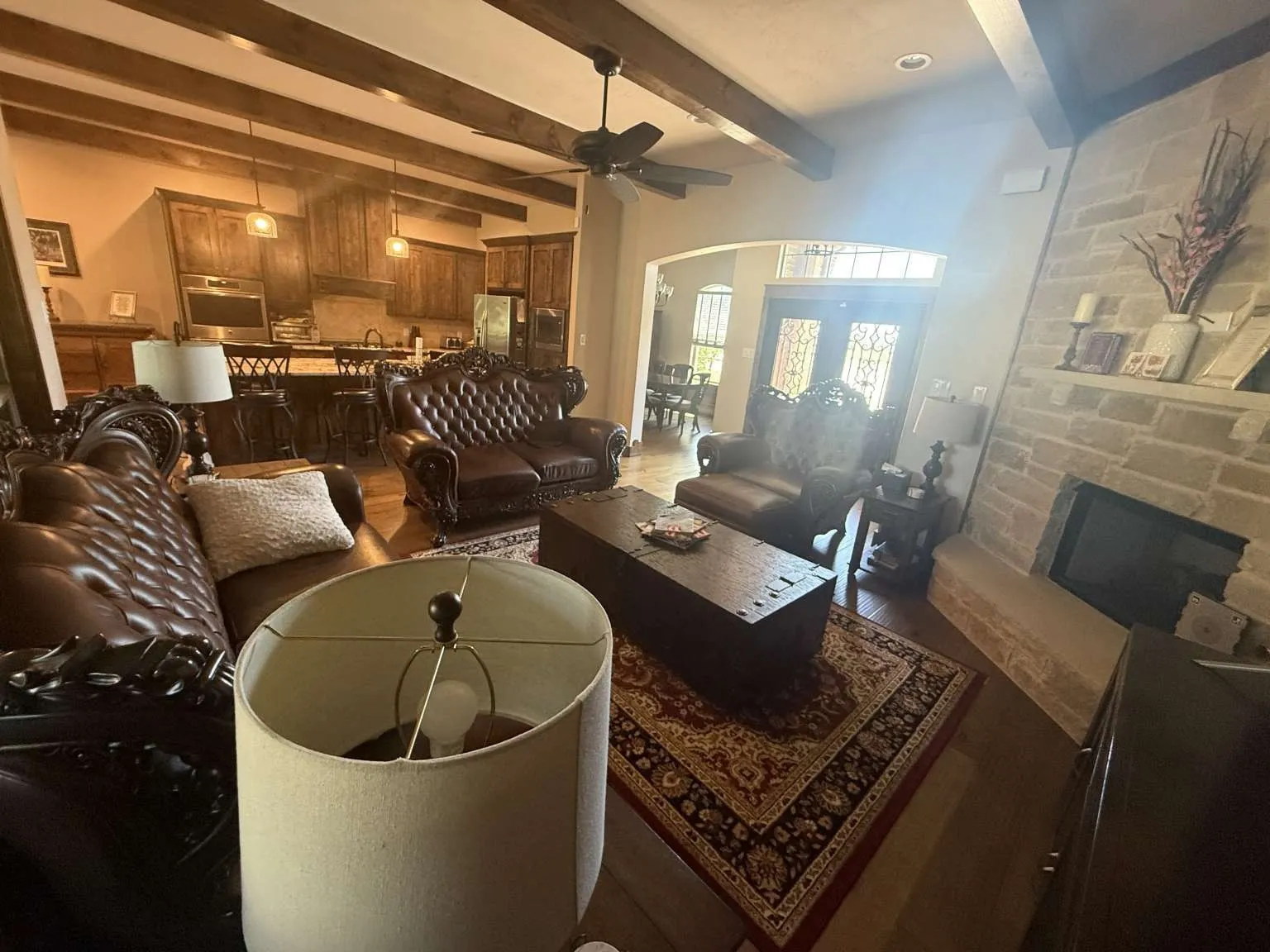 Living room featuring dark wood-style flooring, ceiling fan, arched walkways, beam ceiling, and a fireplace
