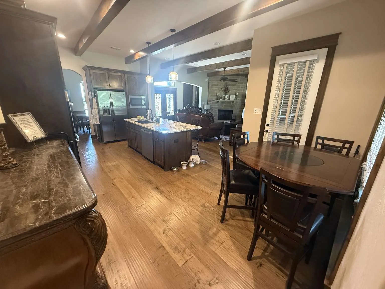 Dining space with beamed ceiling, a fireplace, light wood finished floors, arched walkways, and ceiling fan