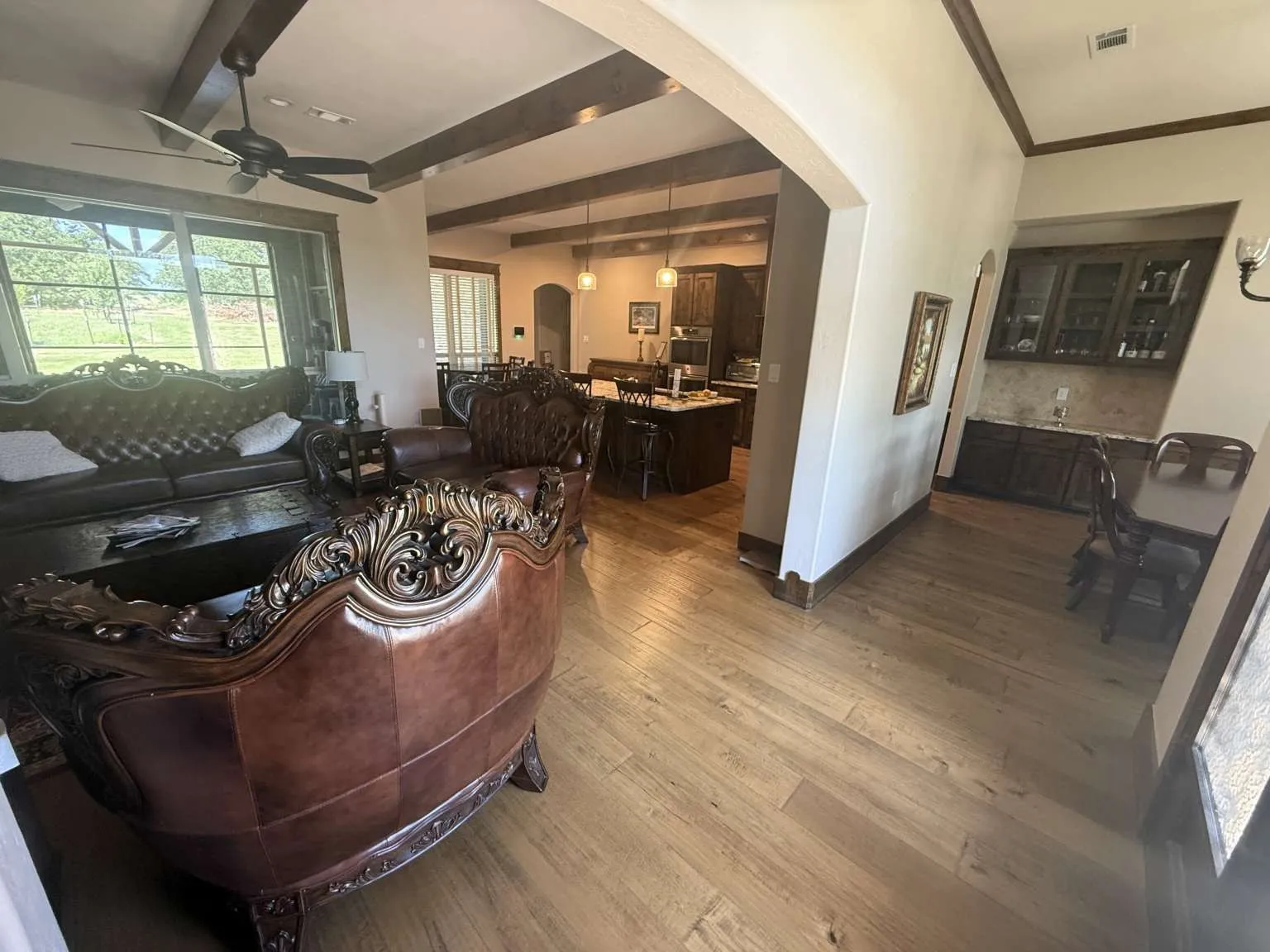Living room with beam ceiling, arched walkways, wood finished floors, ceiling fan, and healthy amount of natural light
