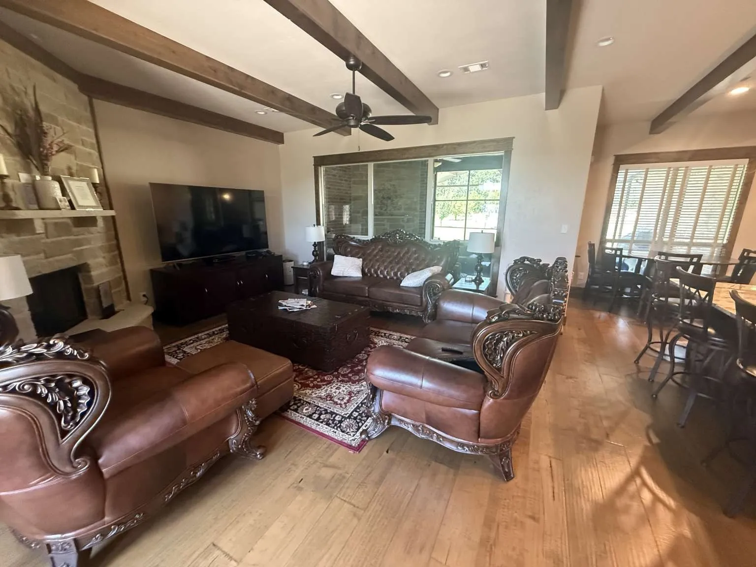 Living area with wood-type flooring, a ceiling fan, beam ceiling, and a fireplace