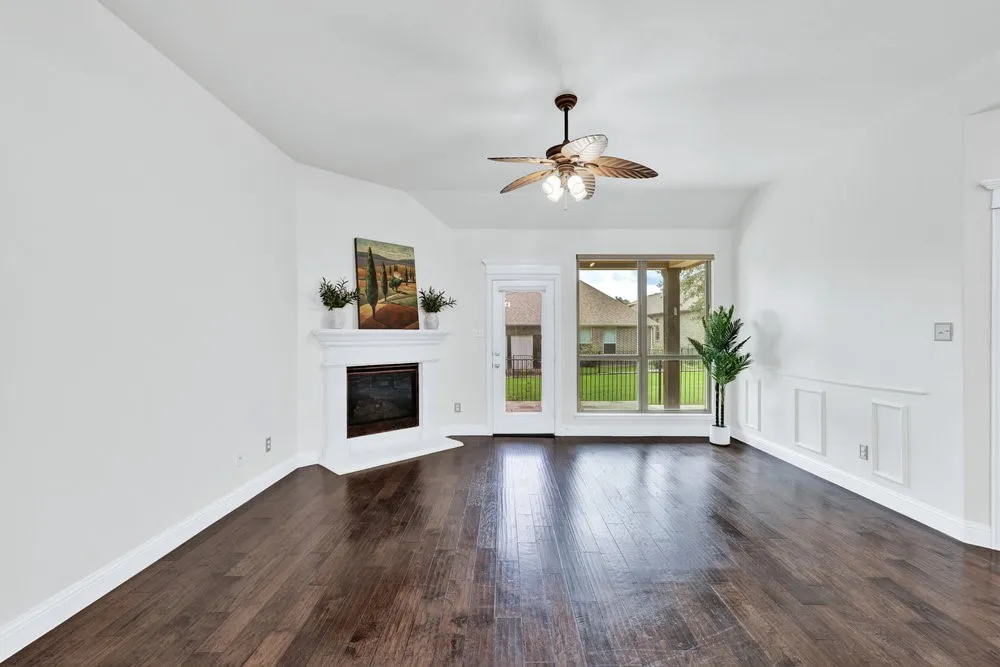 Unfurnished living room with a ceiling fan, a glass covered fireplace, wood finished floors, and vaulted ceiling