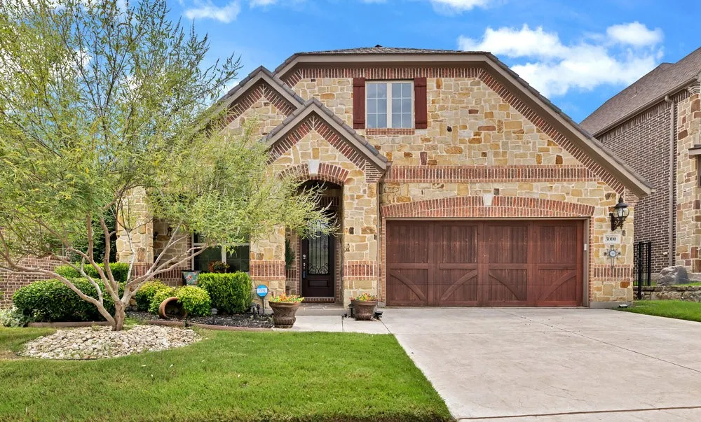 Mediterranean inspired home with stone siding, brick siding, driveway, and a front yard