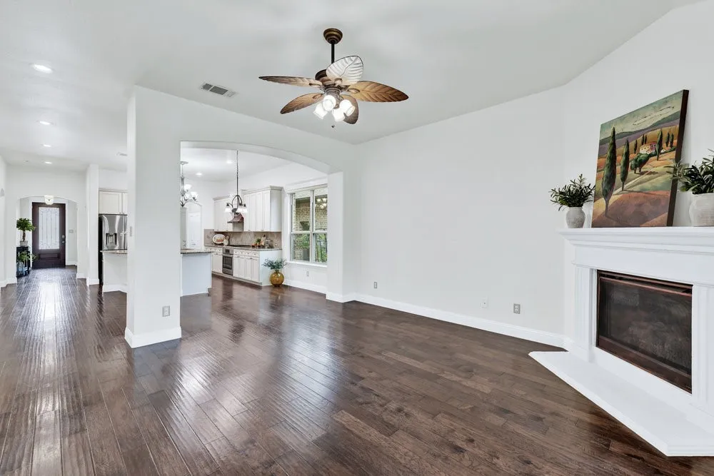 Unfurnished living room featuring arched walkways, a ceiling fan, a glass covered fireplace, a chandelier, and dark wood-style floors