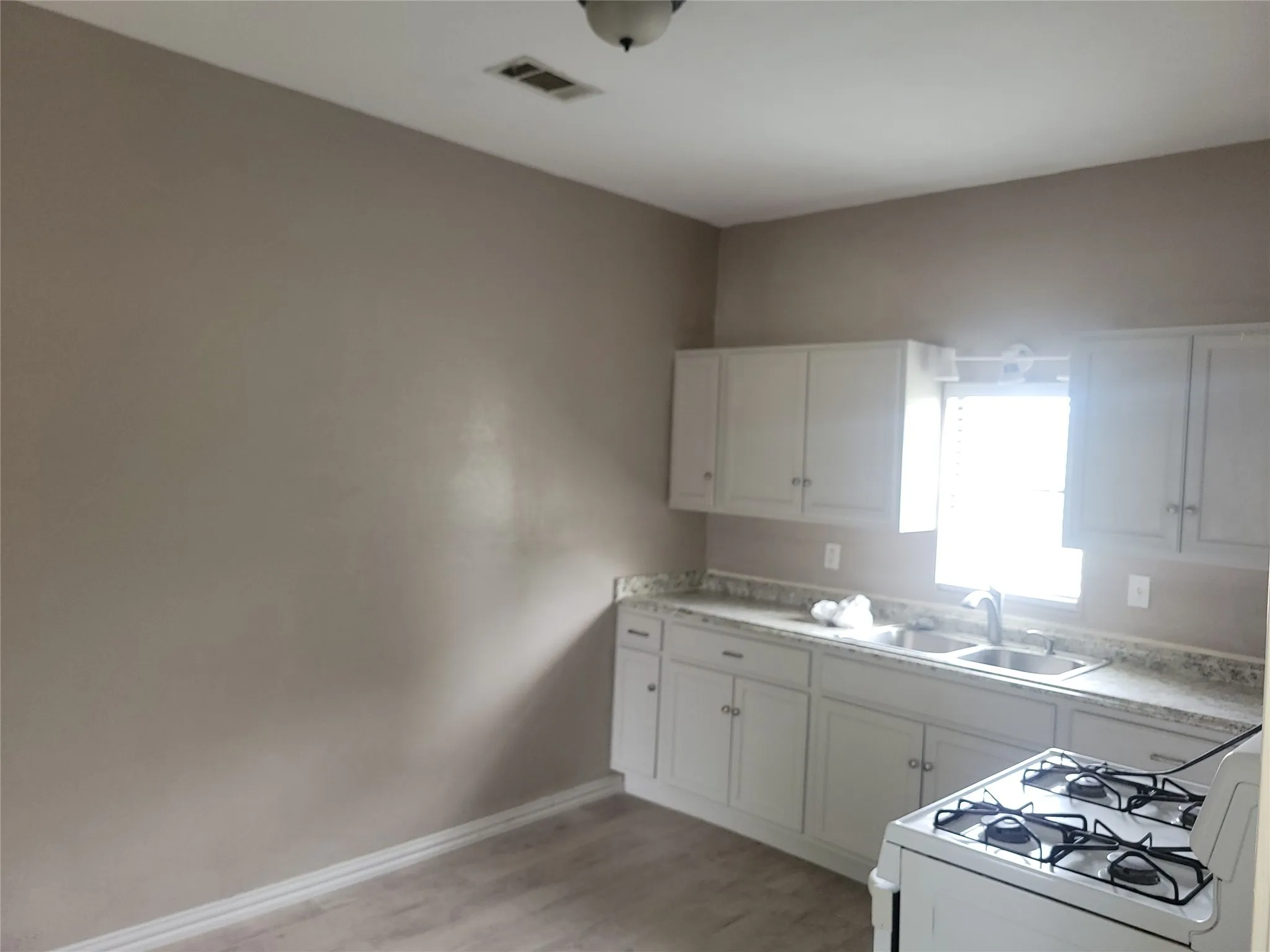 Kitchen featuring white gas range oven, white cabinets, light wood-style flooring, and light countertops