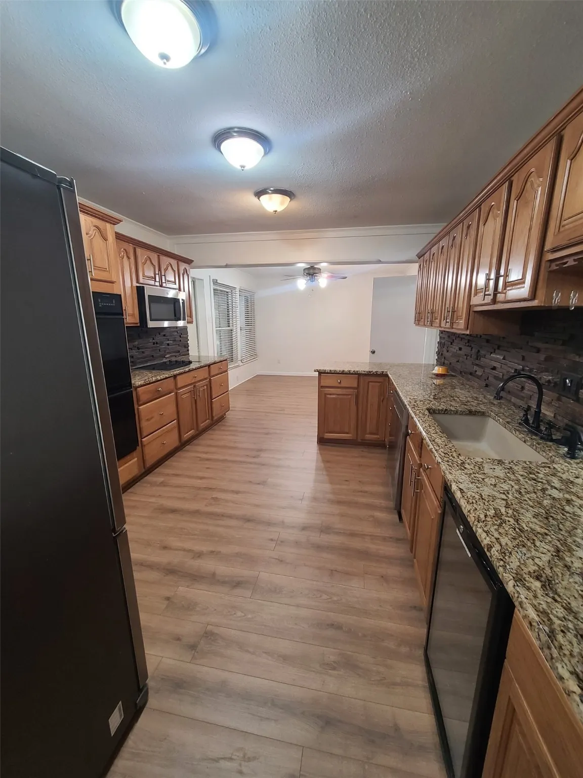 Kitchen featuring decorative backsplash, freestanding refrigerator, a ceiling fan, crown molding, and light stone counters