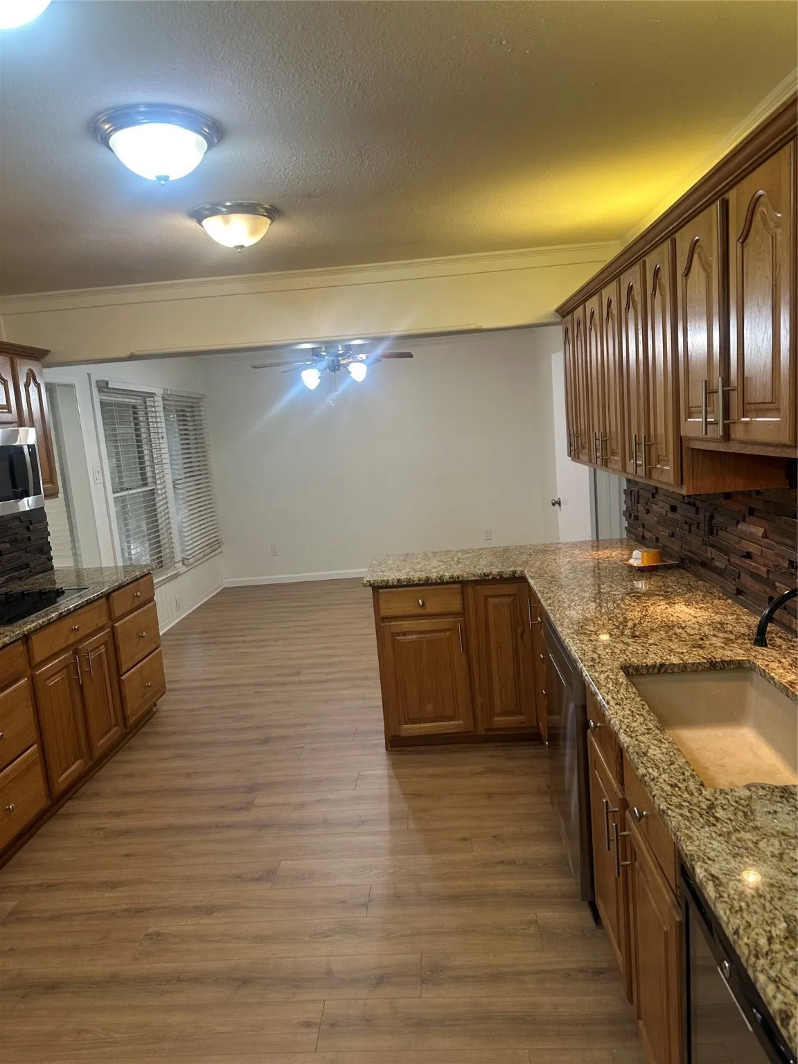 Kitchen with tasteful backsplash, dark wood finished floors, a peninsula, light stone countertops, and a textured ceiling