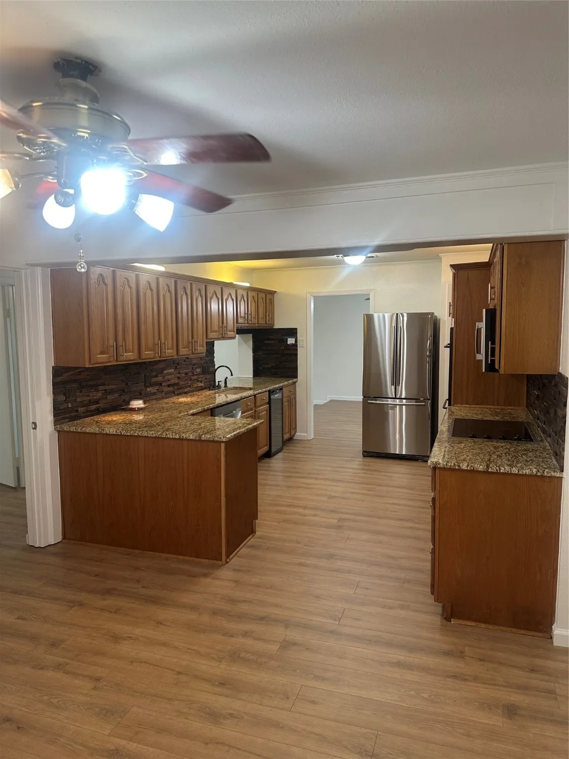 Kitchen featuring tasteful backsplash, a peninsula, refrigerator, light wood-style flooring, and brown cabinetry
