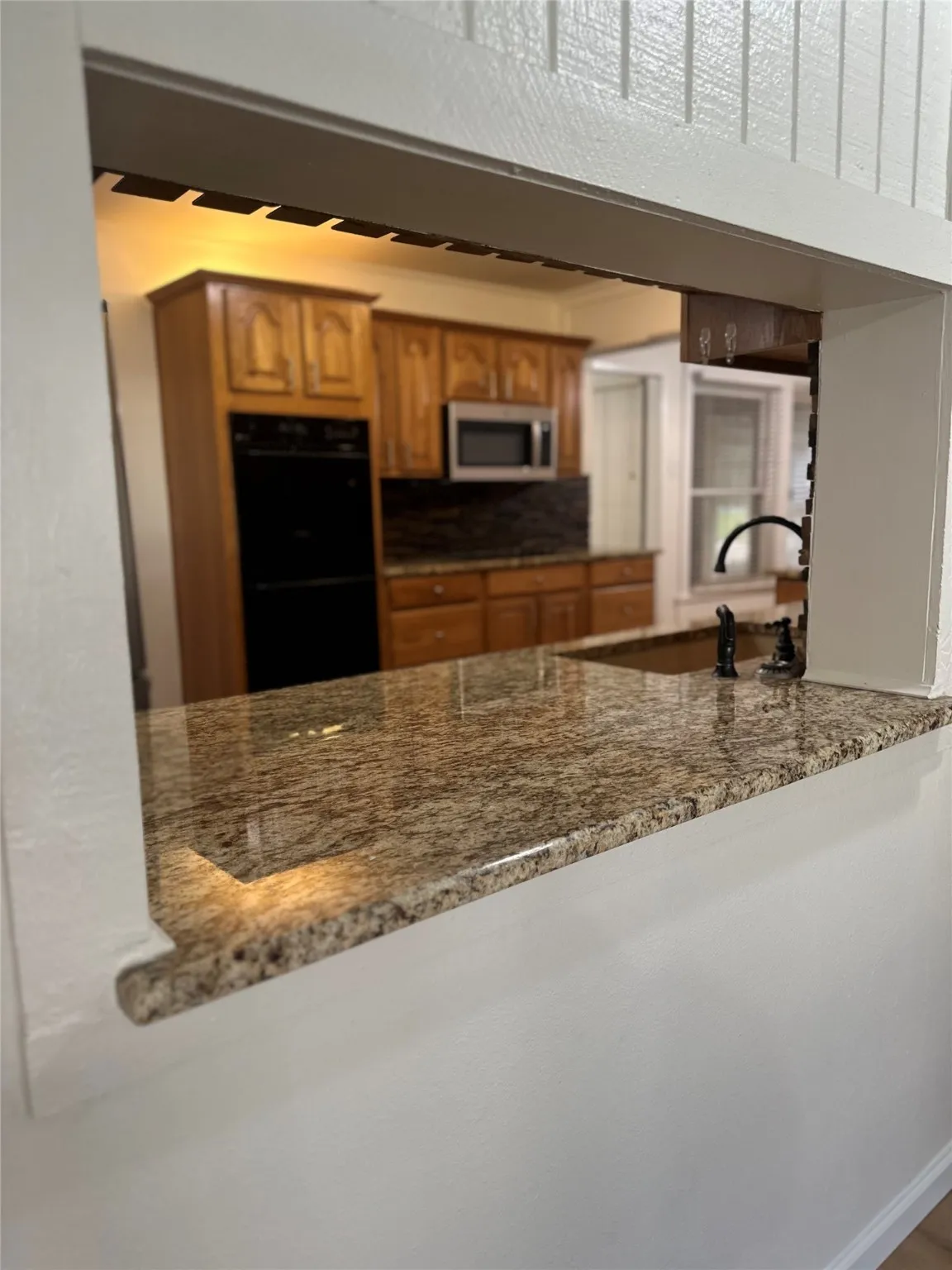 Kitchen with stone counters, brown cabinets, stainless steel microwave, decorative backsplash, and a peninsula