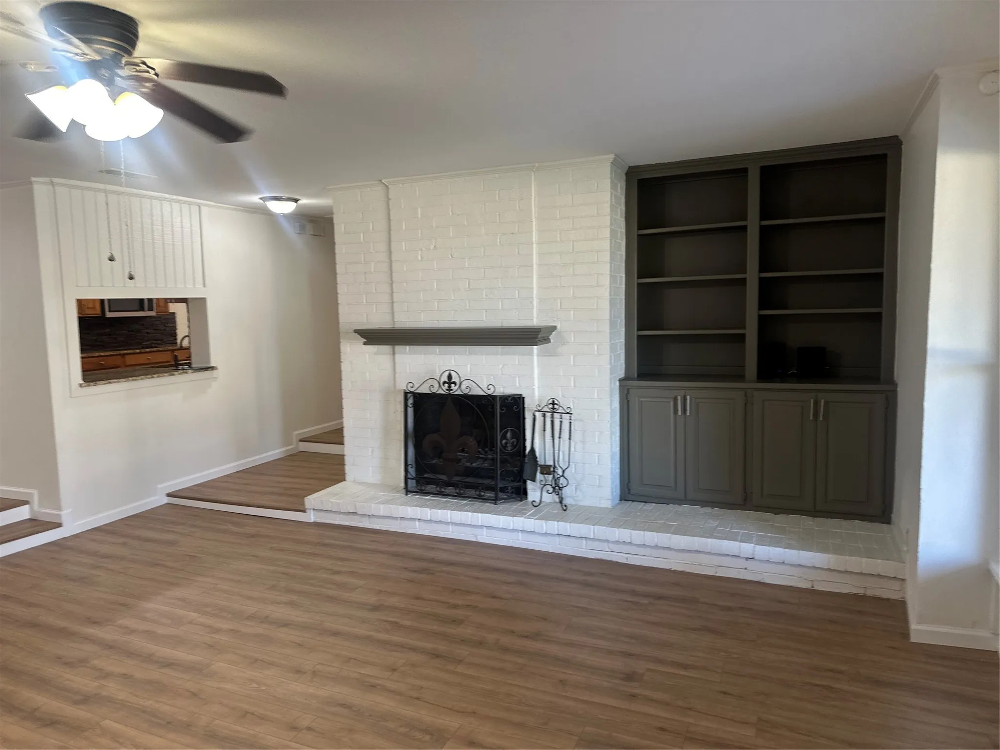 Den with wood finished floors, ceiling fan, and a brick fireplace