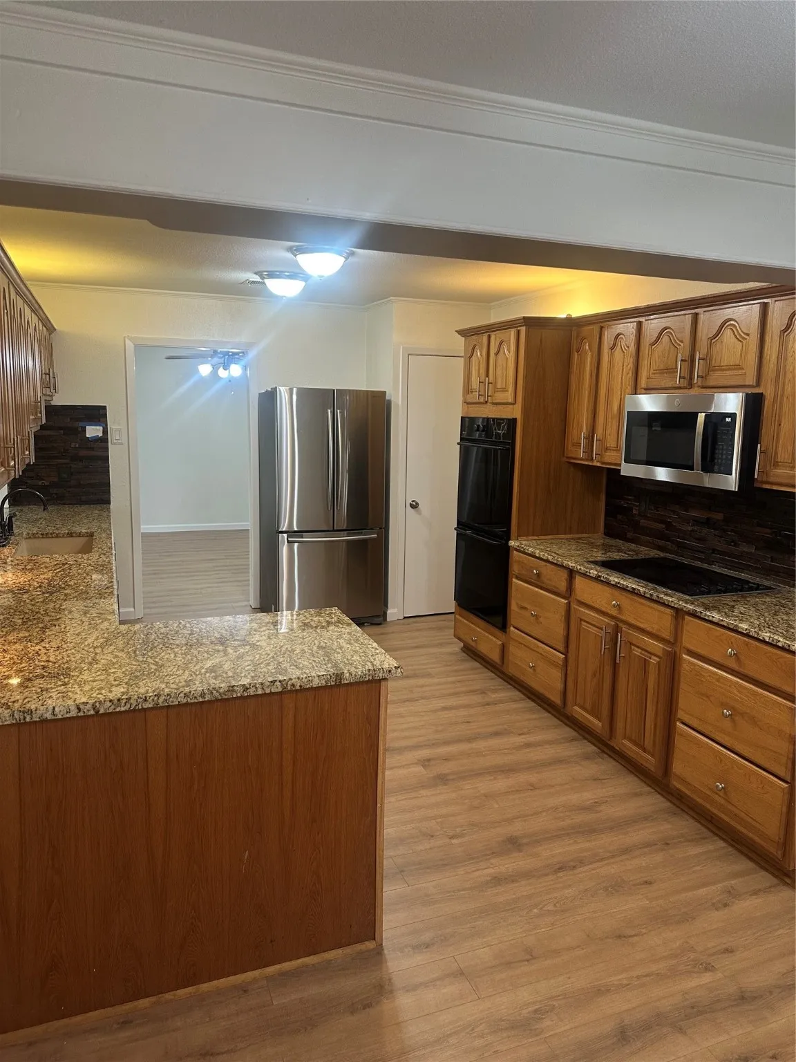 Kitchen featuring stone counters, brown cabinetry, freestanding refrigerator, light wood-style flooring, and crown molding