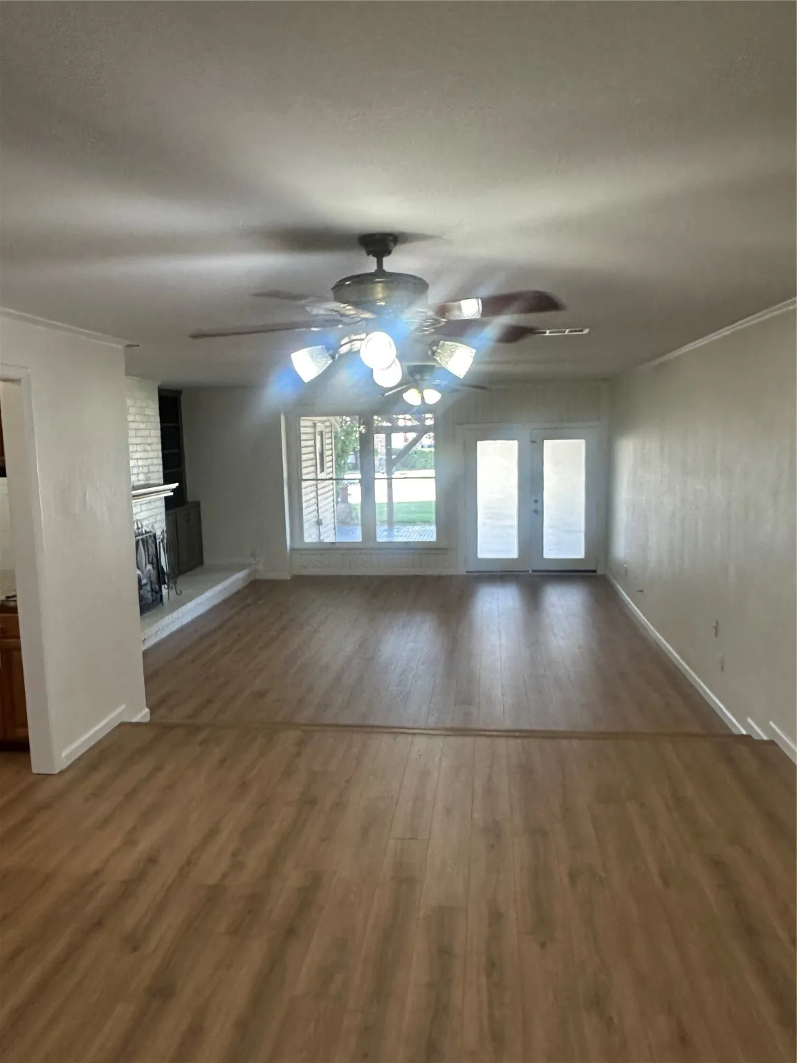 Den with ceiling fan, wood finished floors, a brick fireplace, and ornamental molding
