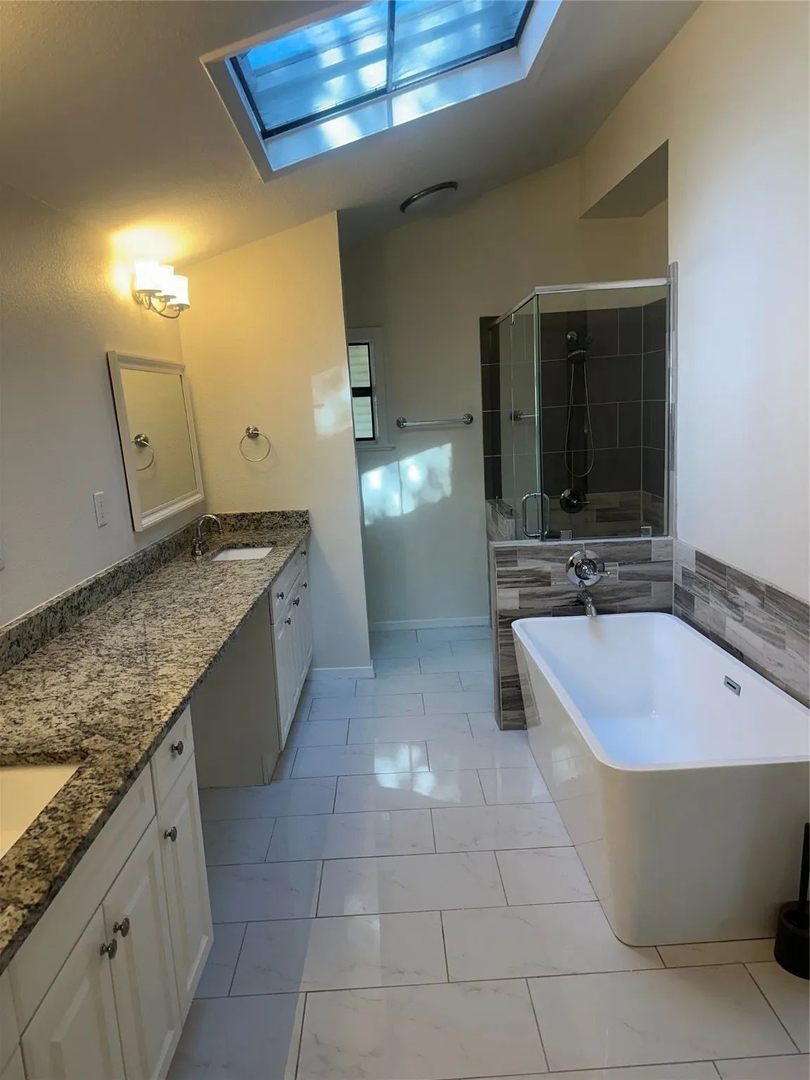 Full bathroom featuring a skylight, double vanity, a stall shower, a soaking tub, and marble look tile flooring
