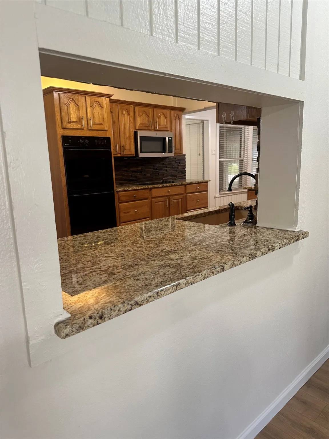 Kitchen with dark stone countertops, dark wood-style flooring, decorative backsplash, brown cabinetry, and multiple ovens