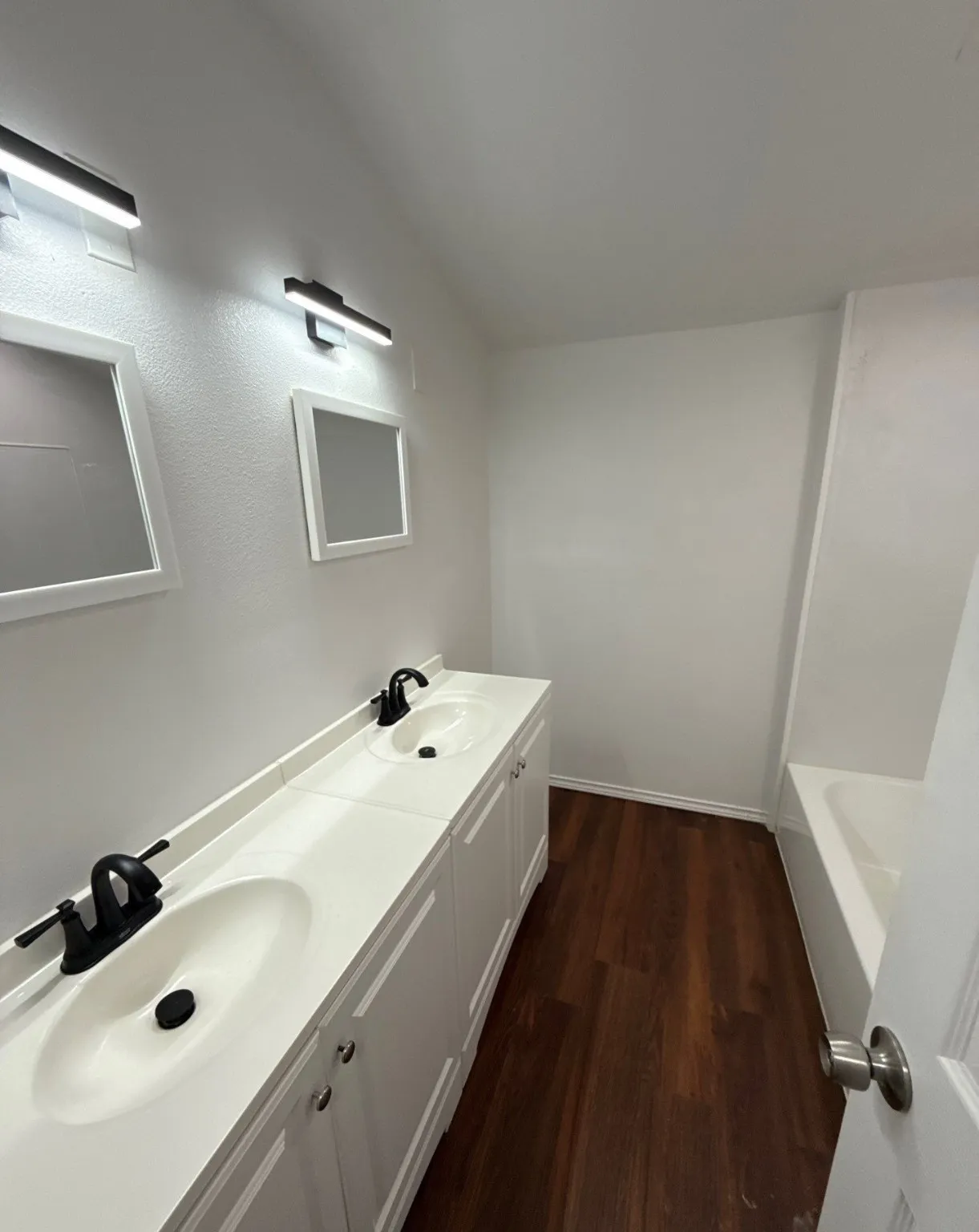 Full bath featuring double vanity, wood finished floors, vaulted ceiling, and a bath