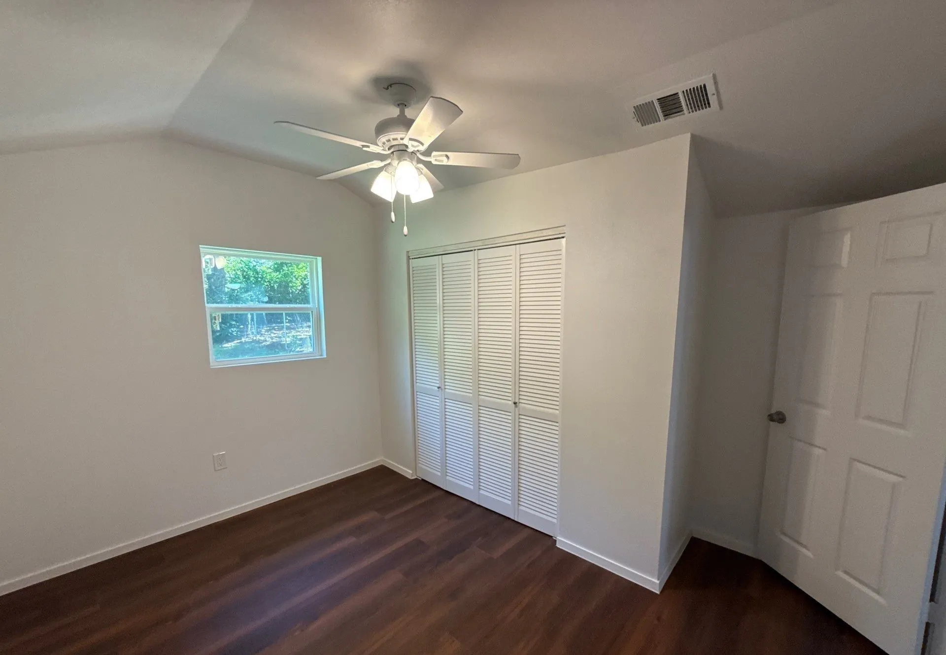 Unfurnished bedroom with a closet, dark wood-style floors, lofted ceiling, and a ceiling fan