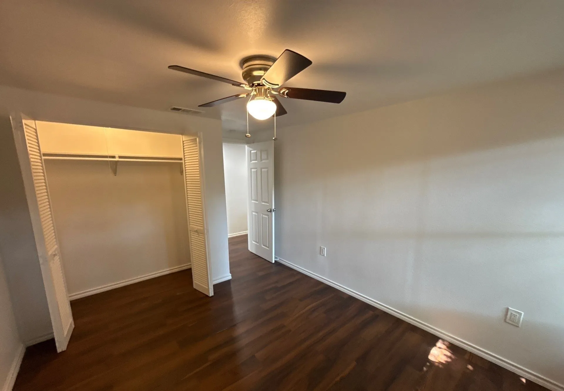 Unfurnished bedroom featuring dark wood-type flooring, a closet, and a ceiling fan