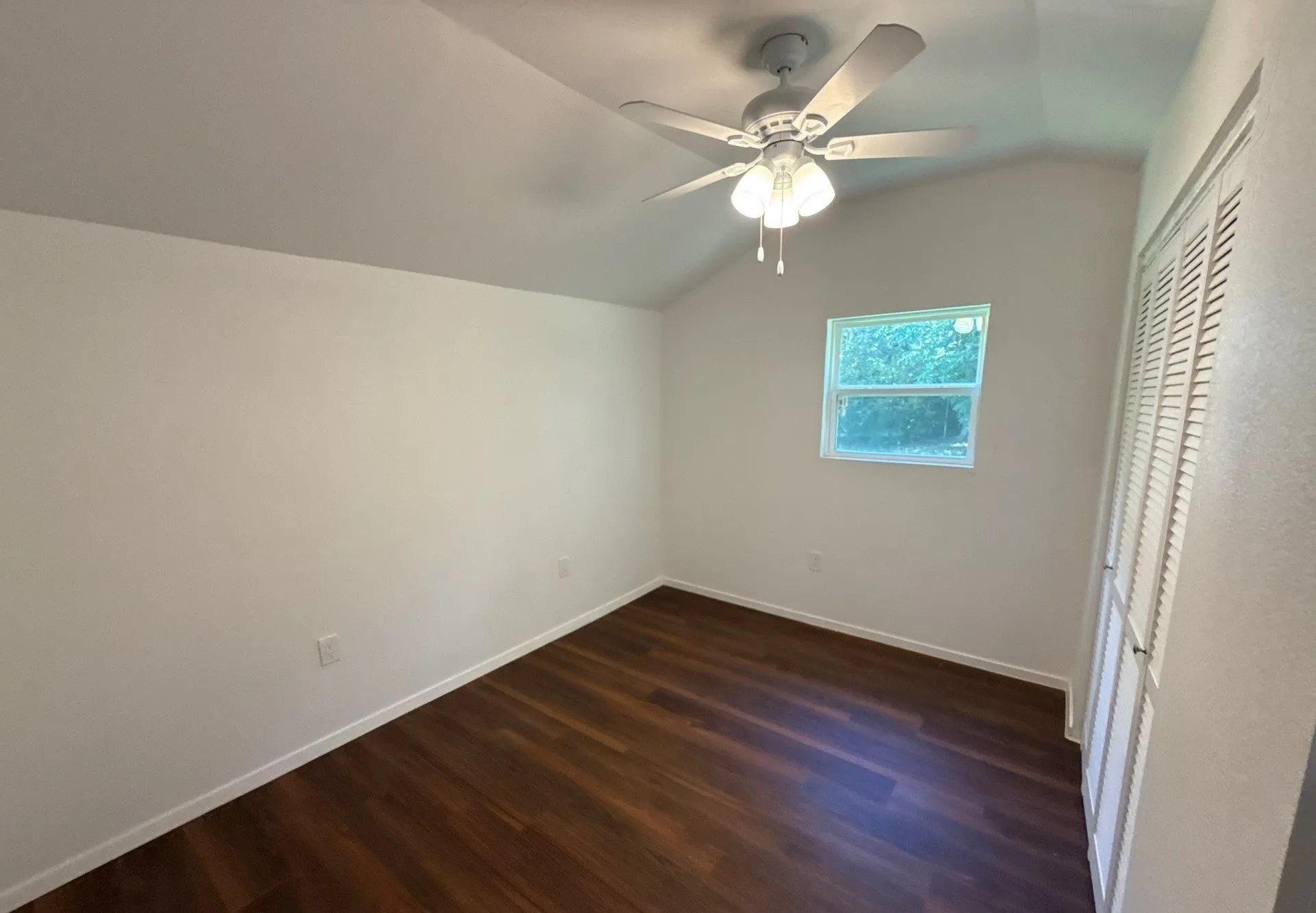 Unfurnished bedroom featuring vaulted ceiling, dark wood-style flooring, and a ceiling fan