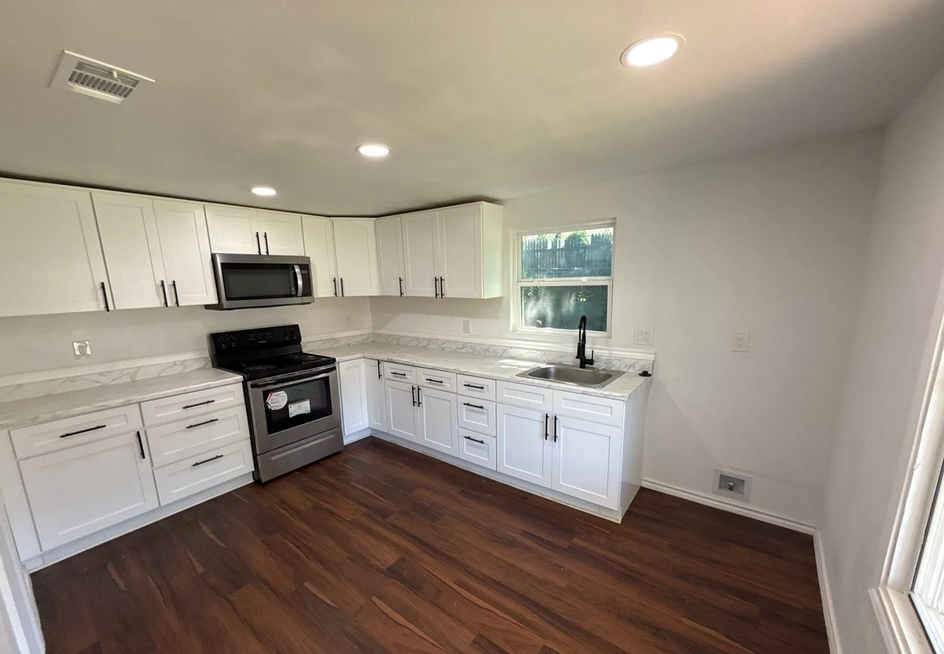 Kitchen with appliances with stainless steel finishes, dark wood-type flooring, recessed lighting, white cabinetry, and light stone countertops