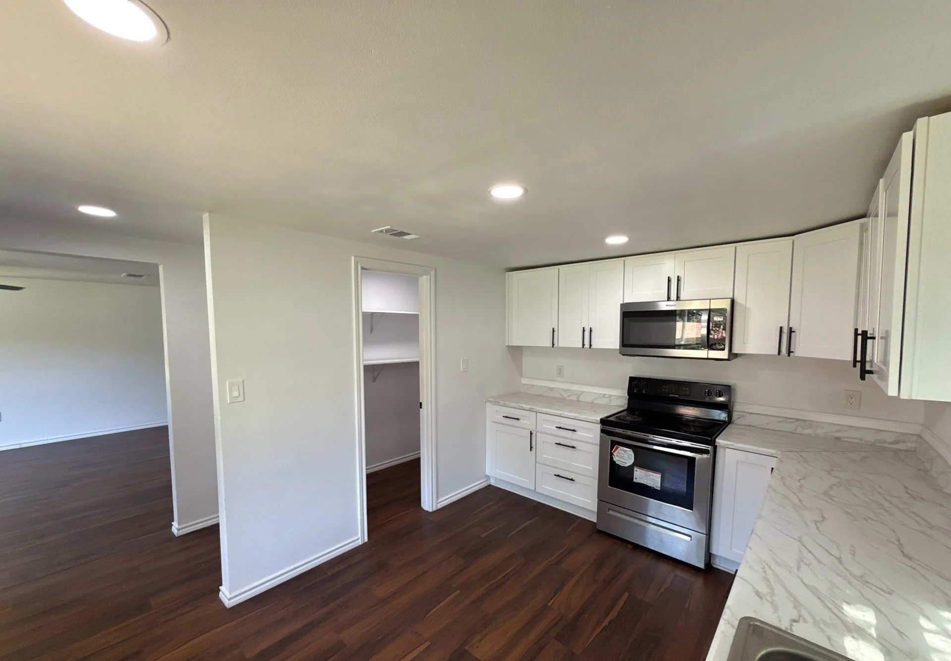 Kitchen with stainless steel appliances, dark wood finished floors, recessed lighting, light stone counters, and white cabinetry